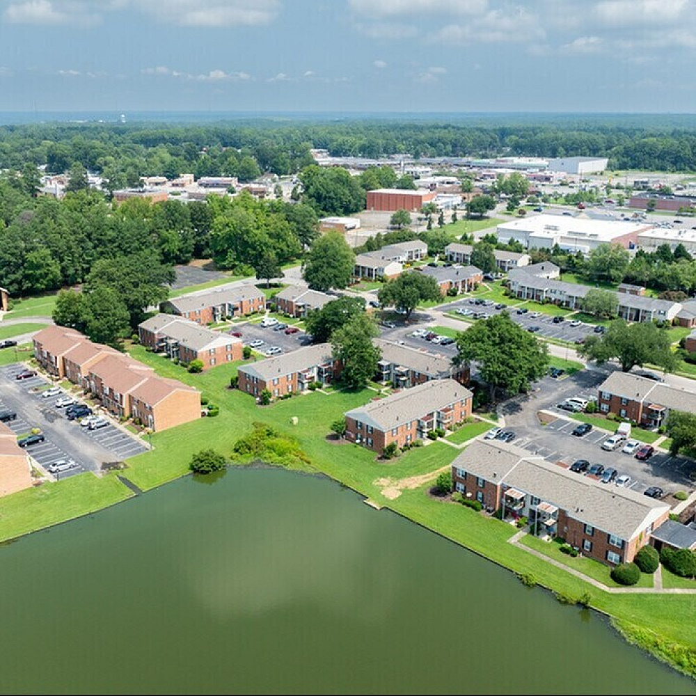 Aerial view of charming apartment complex with red brick buildings, lush green landscaping, and a tranquil pond.