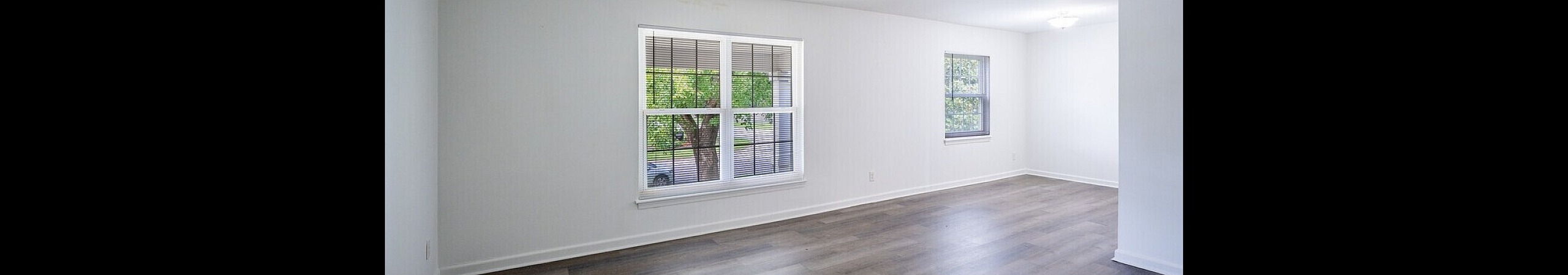 Bright and spacious living area with elegant wood flooring, featuring large windows offering abundant natural light and serene outdoor views.