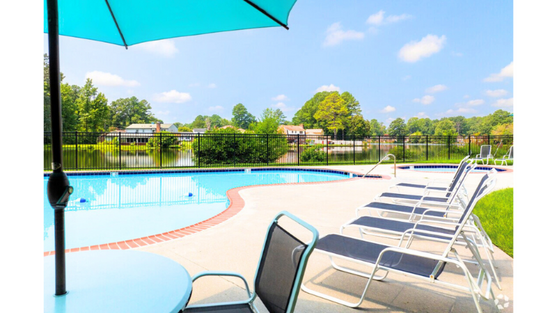 Inviting outdoor pool area with sun loungers, a large umbrella, and serene lake views surrounded by lush greenery.