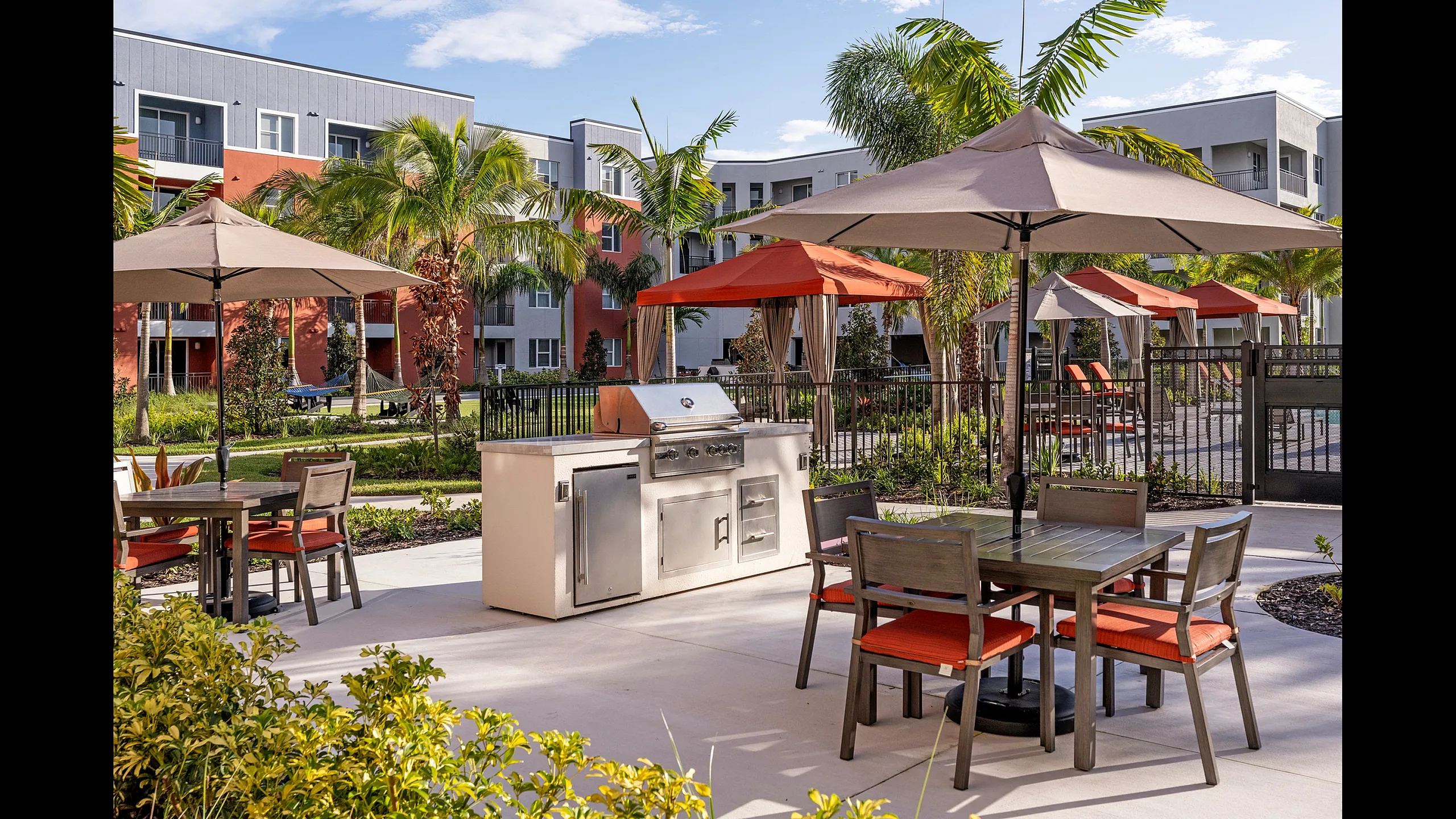 Inviting outdoor patio with a grill, umbrella-shaded tables, and lush landscaping in a modern apartment complex.