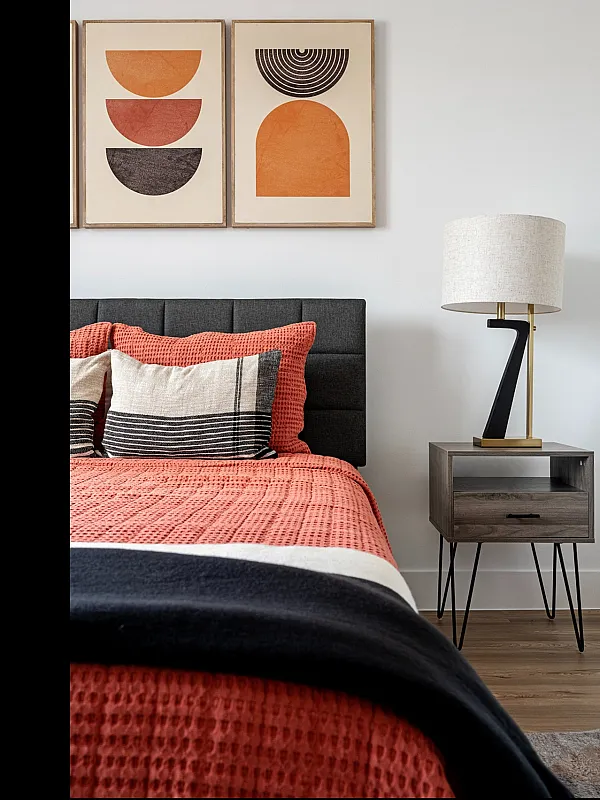 Inviting bedroom with a stylish upholstered bed, warm coral bedding, geometric artwork, and a contemporary nightstand with a modern lamp.