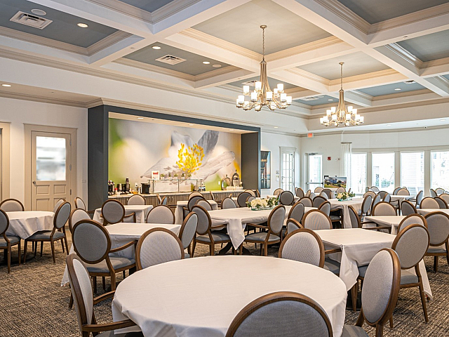 Elegant dining area in a luxurious apartment community, featuring stylish round tables with graceful chandeliers and modern decor.