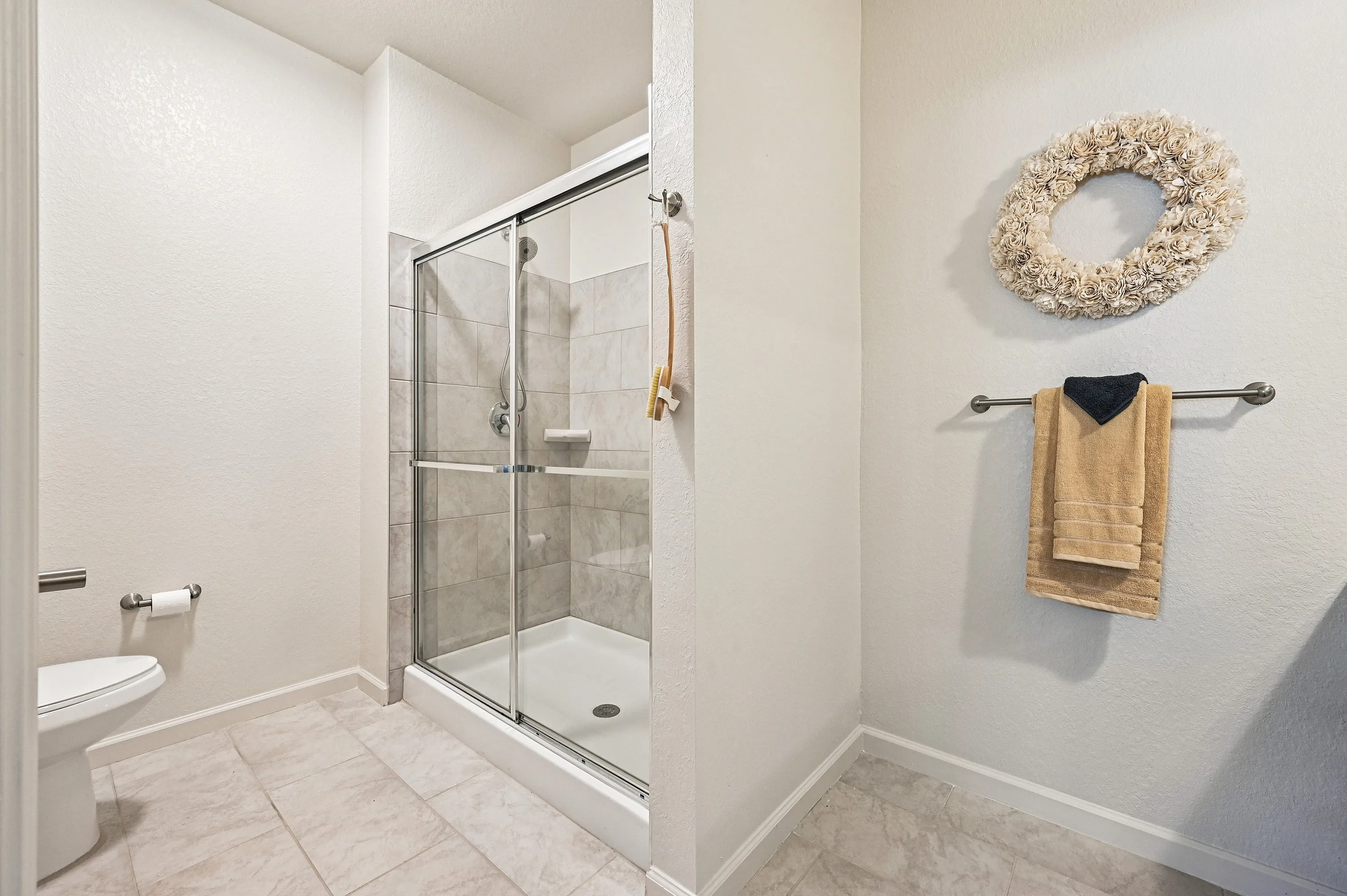 Modern bathroom with elegant glass shower, neutral tile flooring, and decorative floral wall accent.