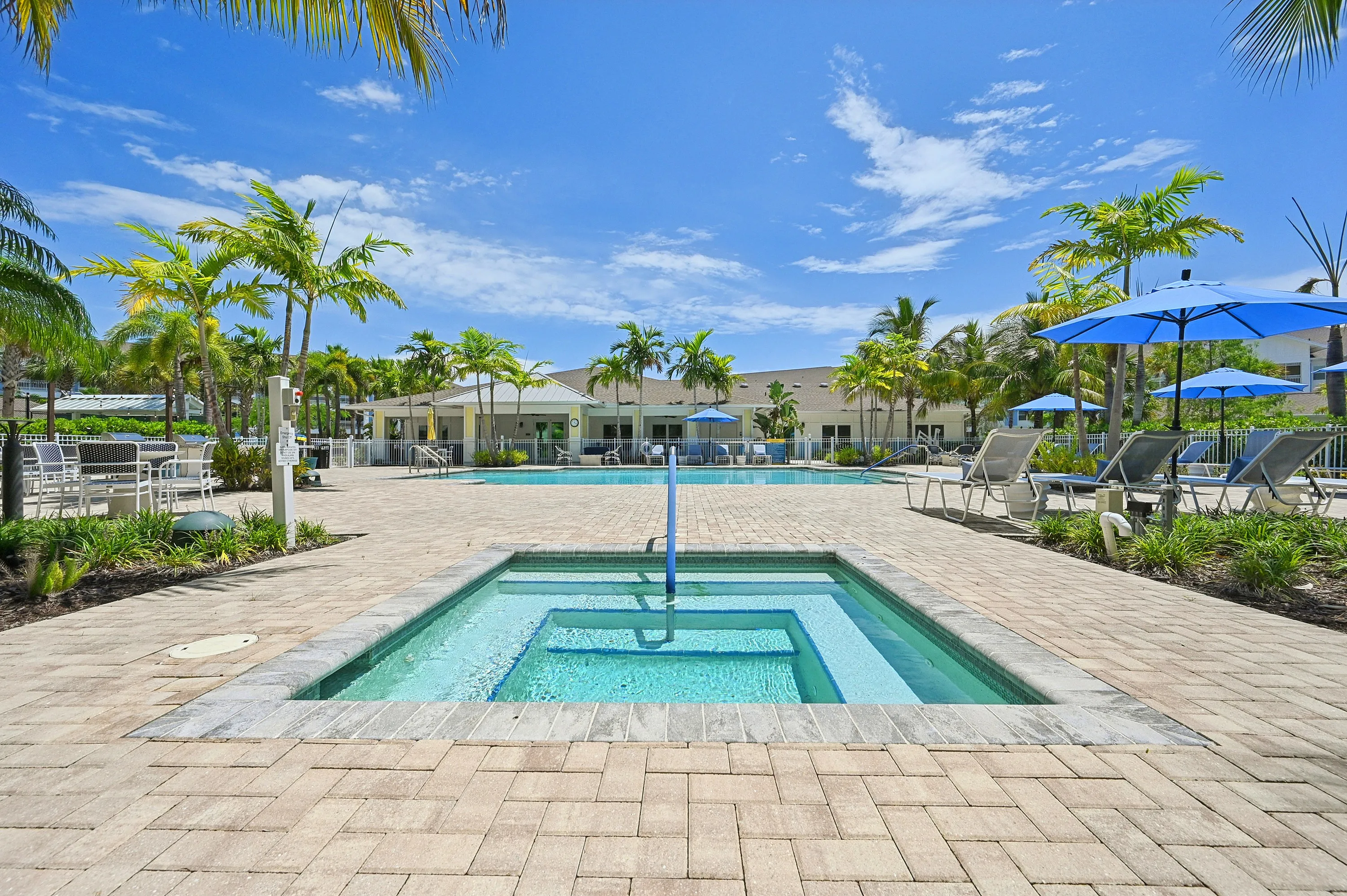 Luxurious outdoor pool area with palm trees, sun loungers, and vibrant blue umbrellas against a clear sky.
