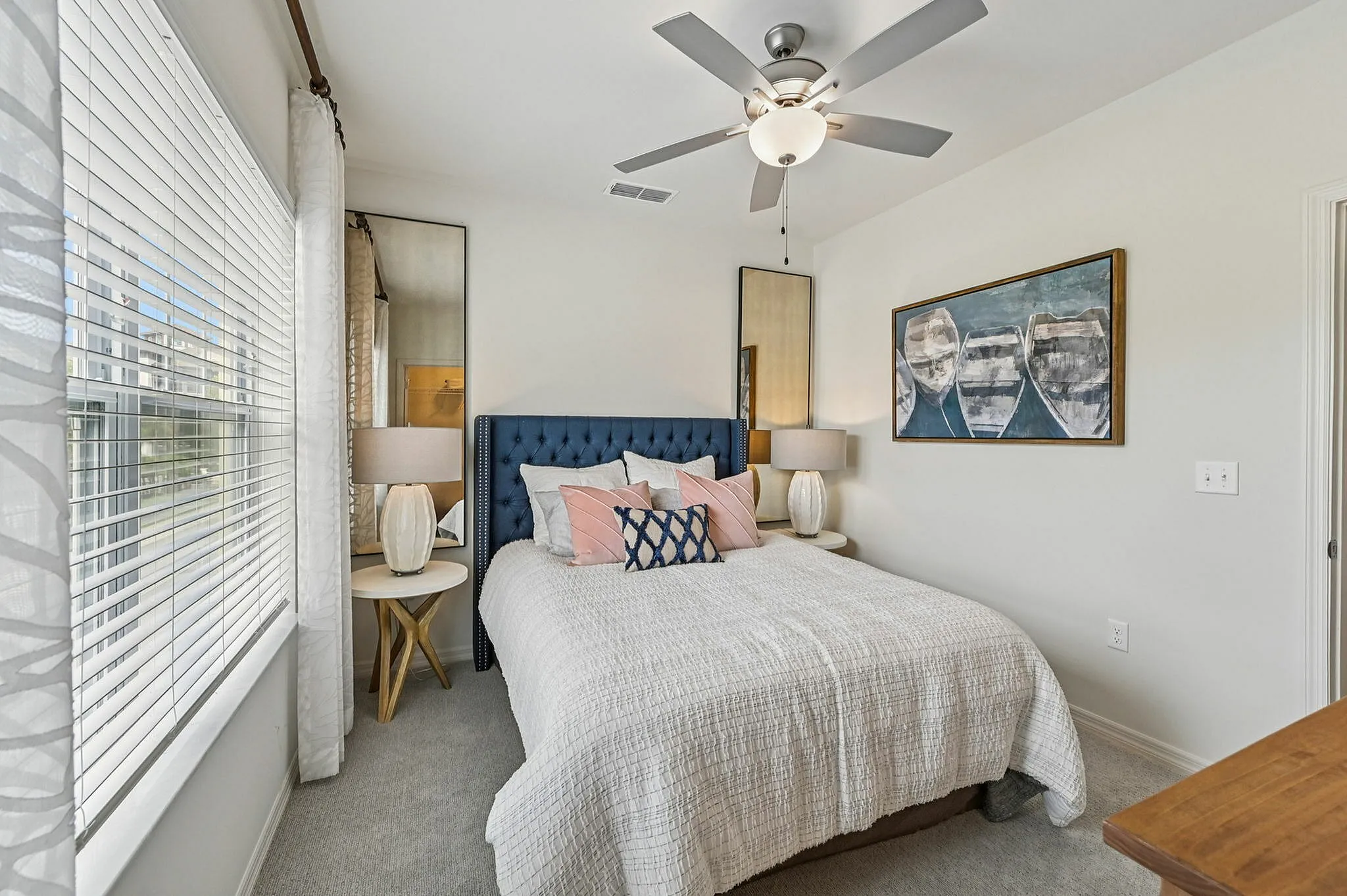Elegant bedroom with a plush blue headboard, stylish decor, large window, and ceiling fan for a cozy ambiance.