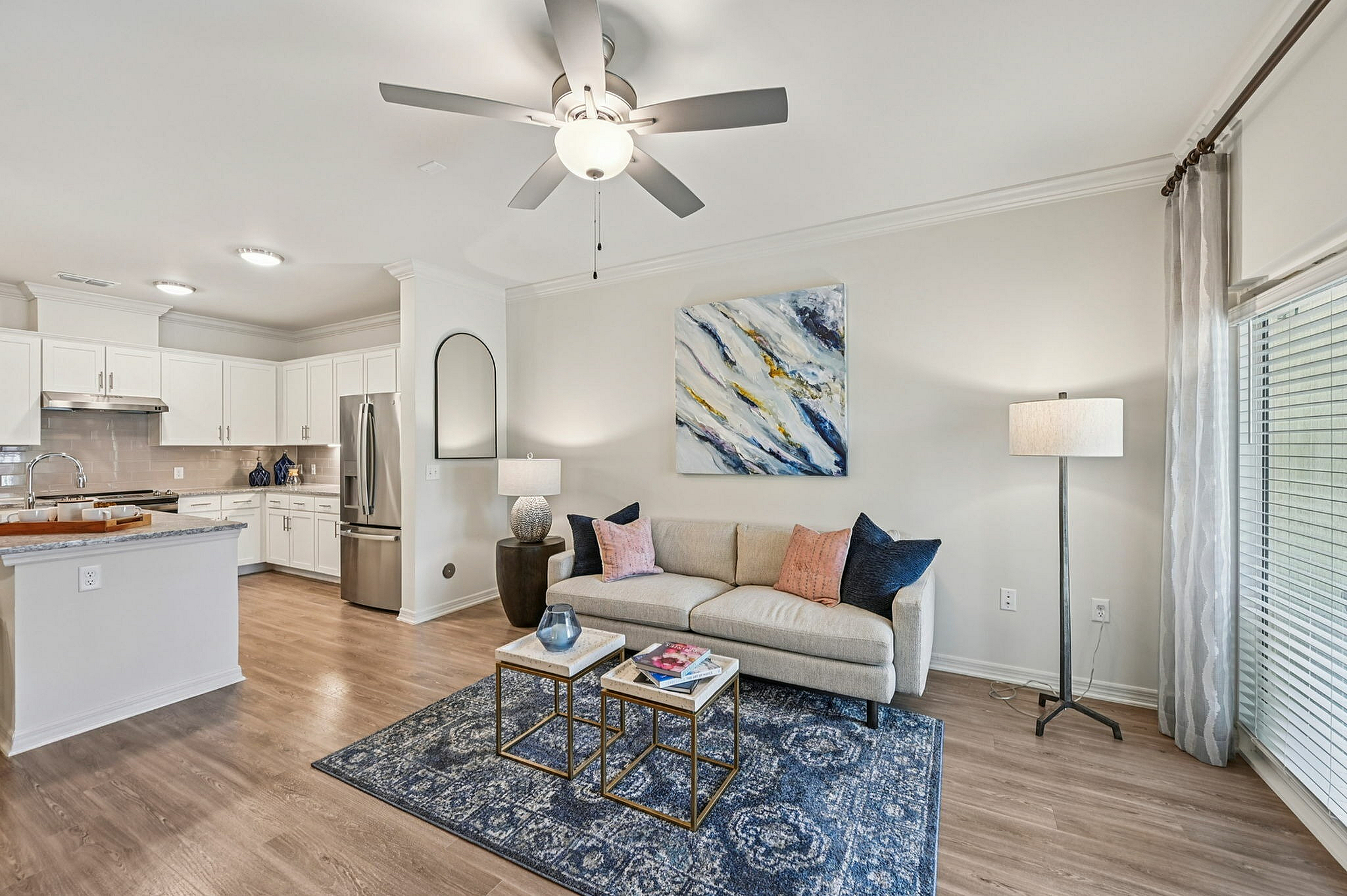 Chic open-plan living area with elegant kitchen and cozy seating, highlighted by a stylish ceiling fan and large windows for natural light.