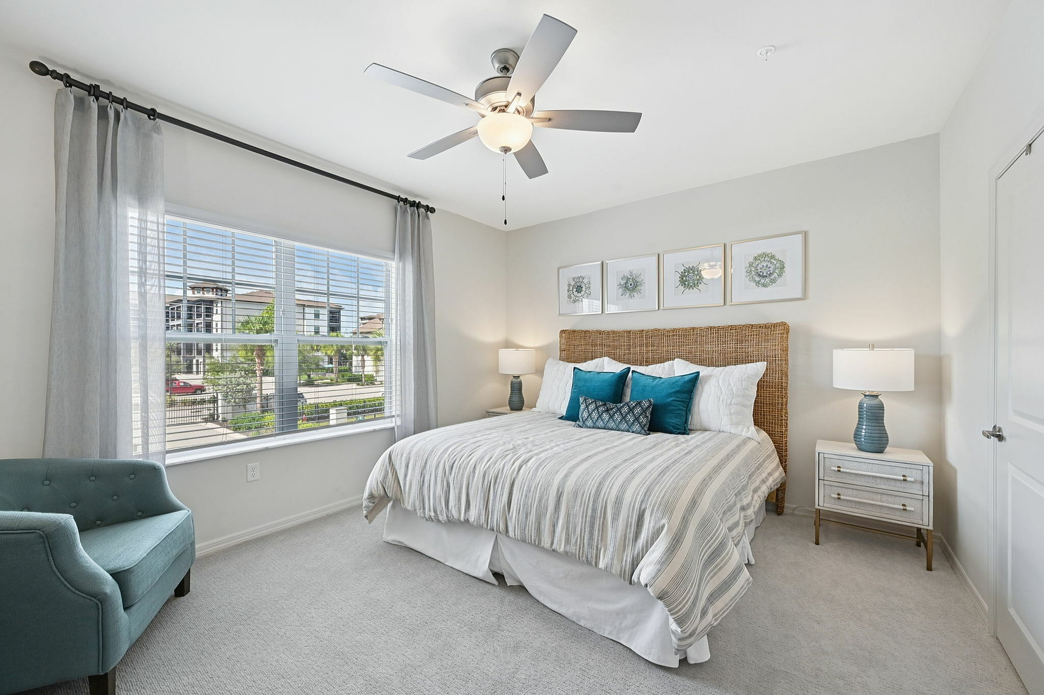 Bright and airy bedroom with elegant decor, featuring a plush bed with striped bedding, stylish lamps, and a comfortable teal armchair by a large window.