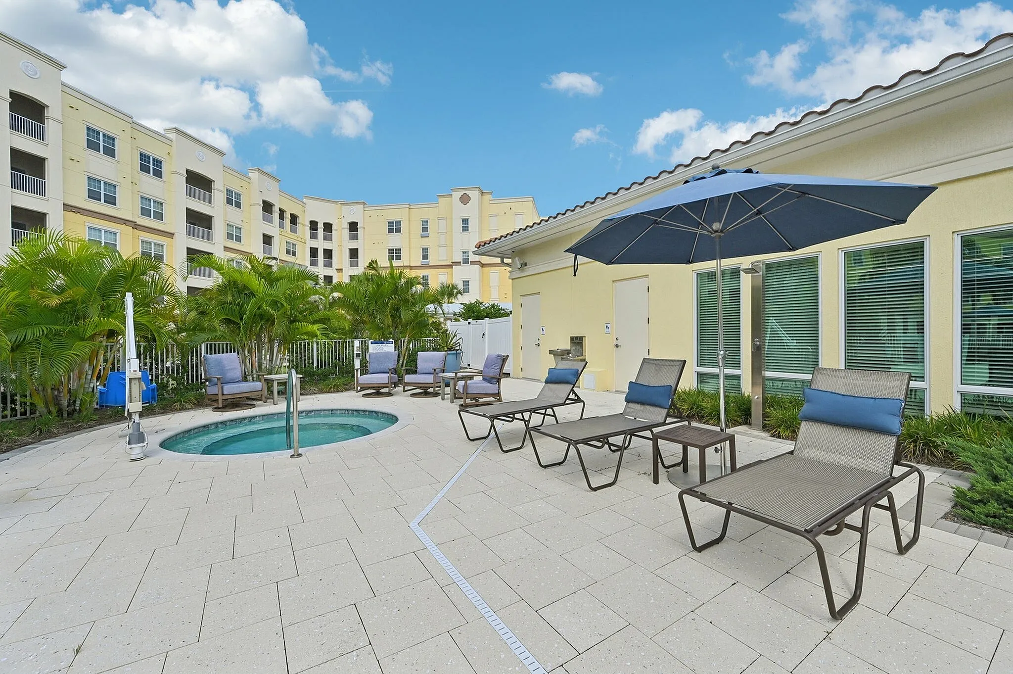Inviting apartment complex courtyard featuring a cozy hot tub, stylish sun loungers, and lush greenery against a bright and welcoming building facade.