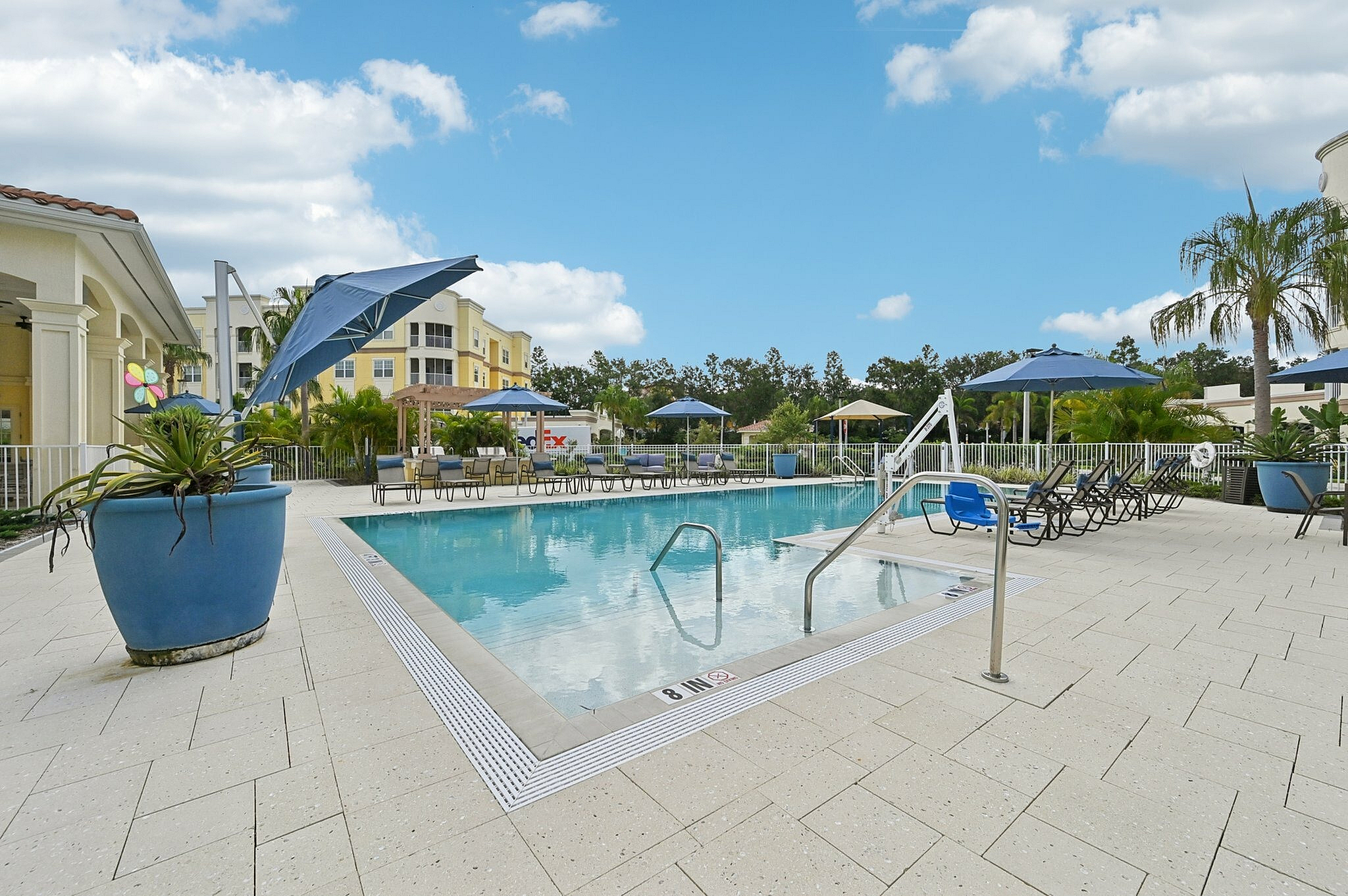 Inviting outdoor pool area with stylish lounge chairs and vibrant blue umbrellas set against a clear sky, perfect for relaxation and leisure.