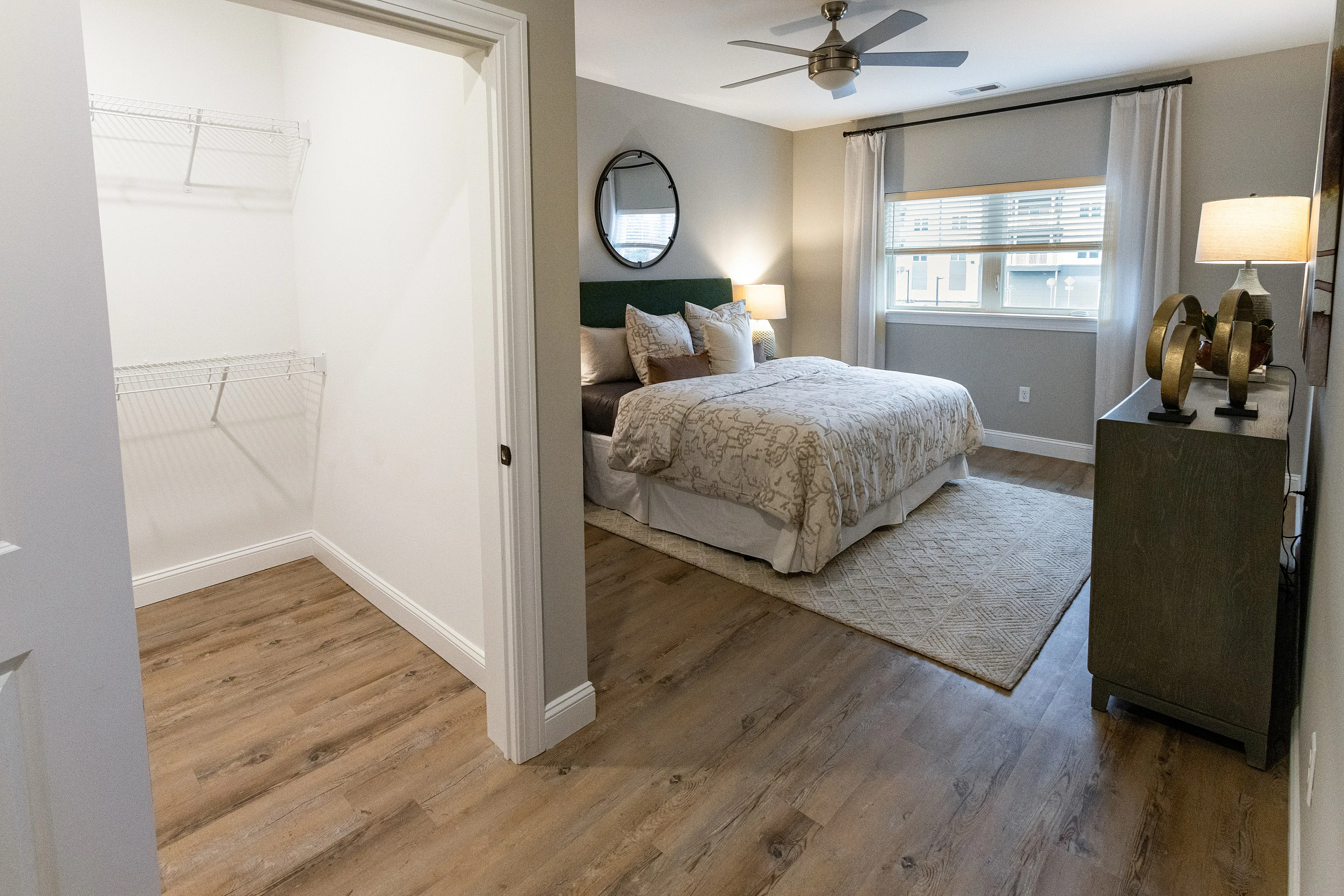 Inviting bedroom with cozy bedding, elegant decor, and a spacious walk-in closet, featuring natural light and warm wood flooring.