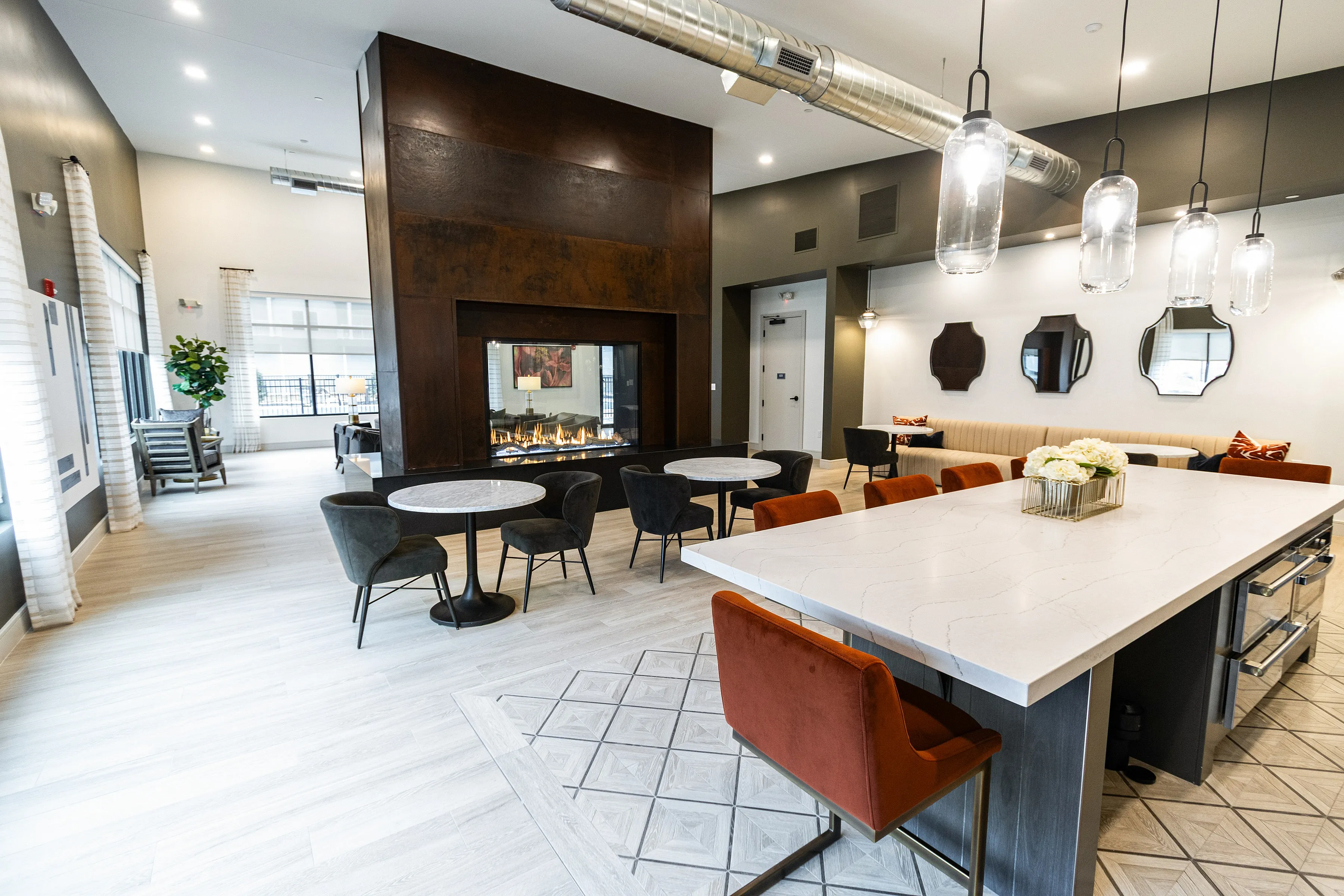 Modern communal space featuring a chic fireplace, elegant dining tables, and stylish pendant lighting, perfect for entertaining or relaxing.