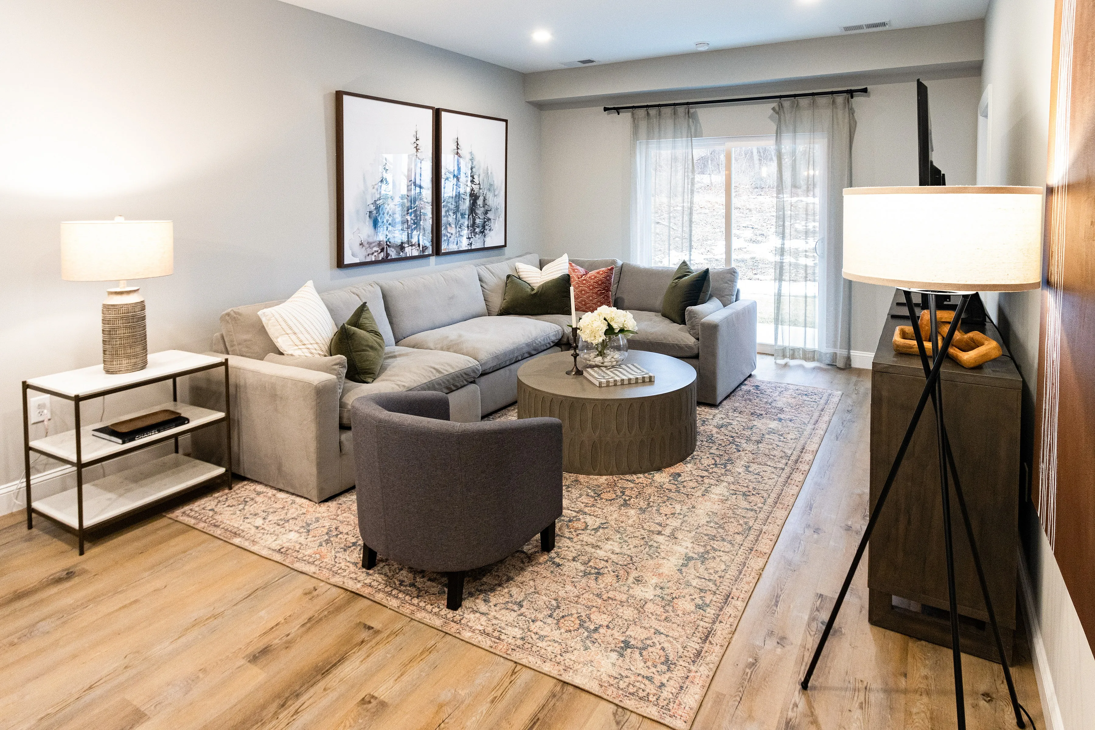 Inviting living room with elegant decor, soft gray sectional, modern armchairs, stylish lighting, and a beautiful view through large sliding glass doors.