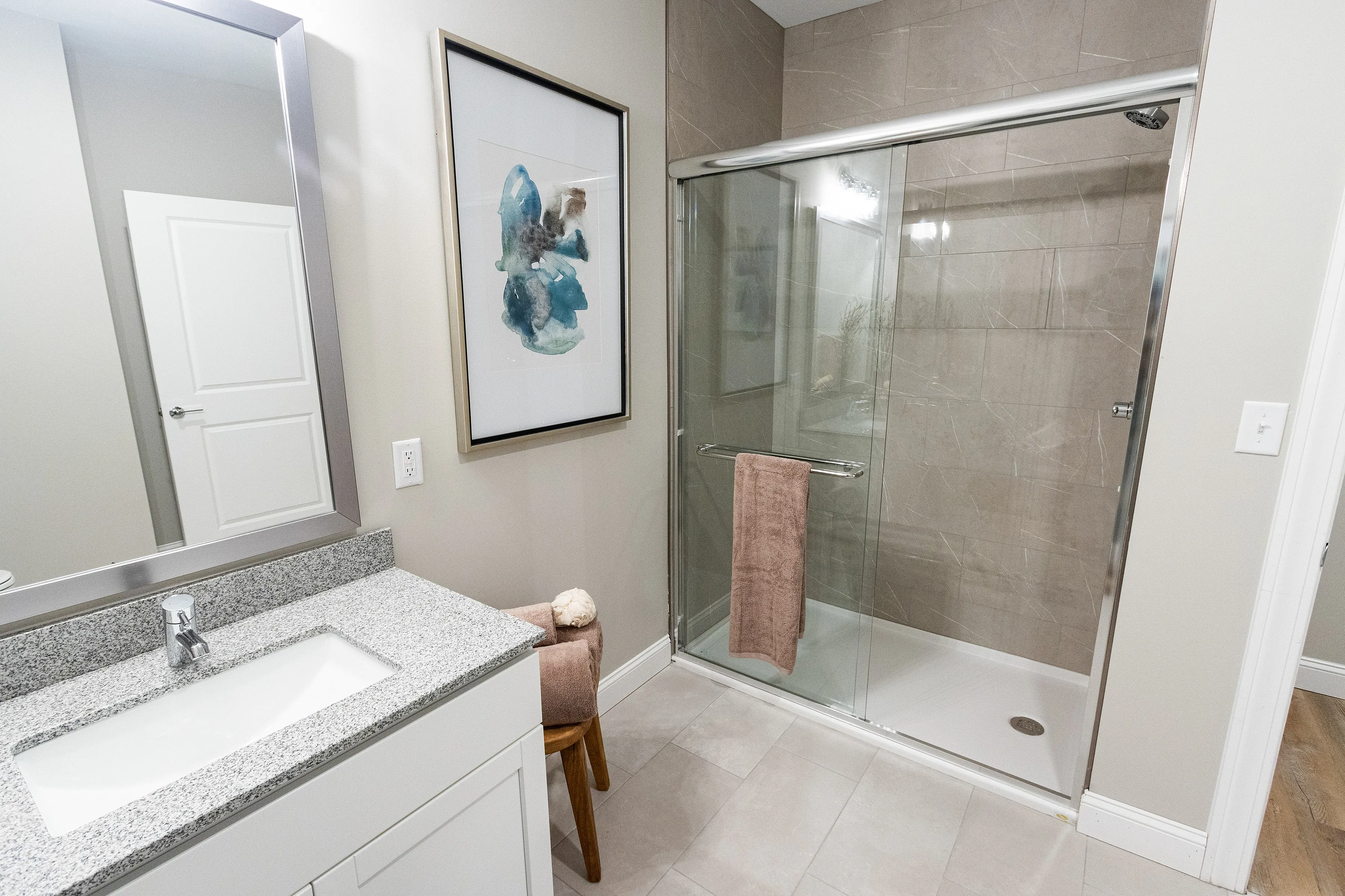 Modern bathroom featuring a sleek glass shower, elegant artwork, and a stylish granite countertop.