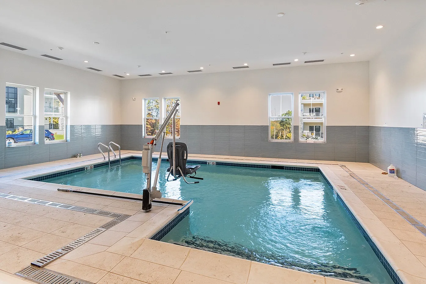 Modern indoor swimming pool with sleek tile flooring and abundant natural light from large windows.