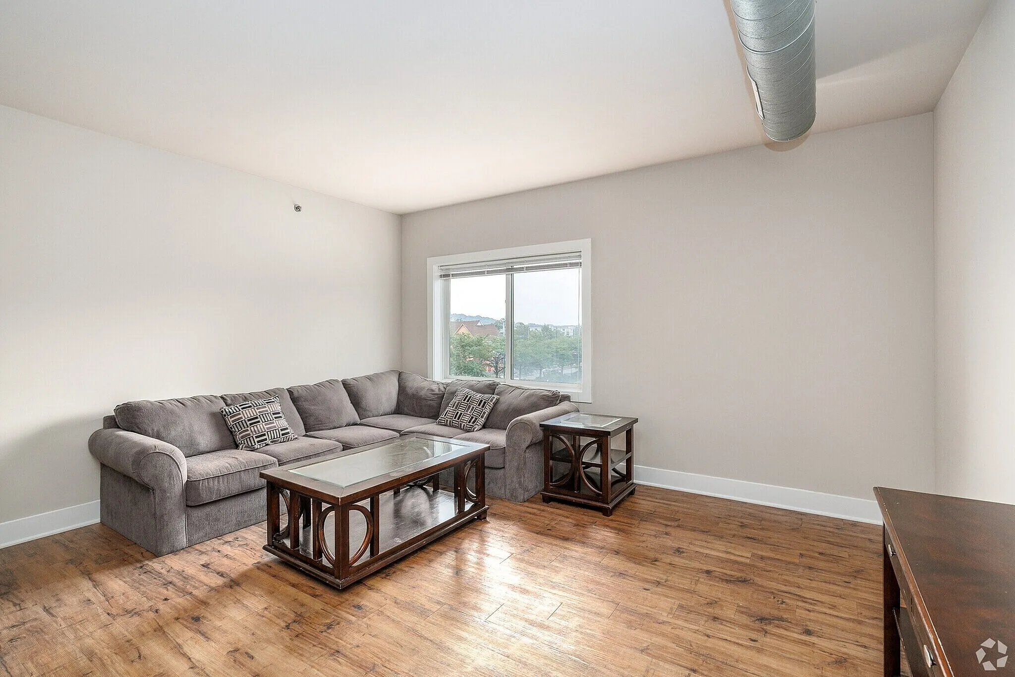 Bright and inviting living room with a plush gray sectional sofa, elegant wooden tables, and sleek hardwood floors, perfect for relaxation and entertaining.