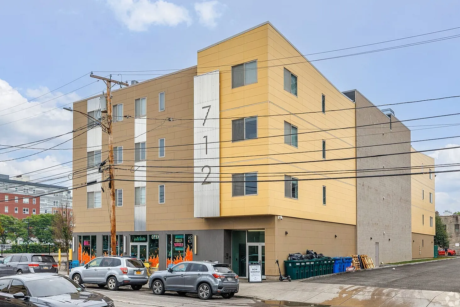 Modern yellow apartment building with street-facing windows and ground-floor businesses, offering contemporary urban living.