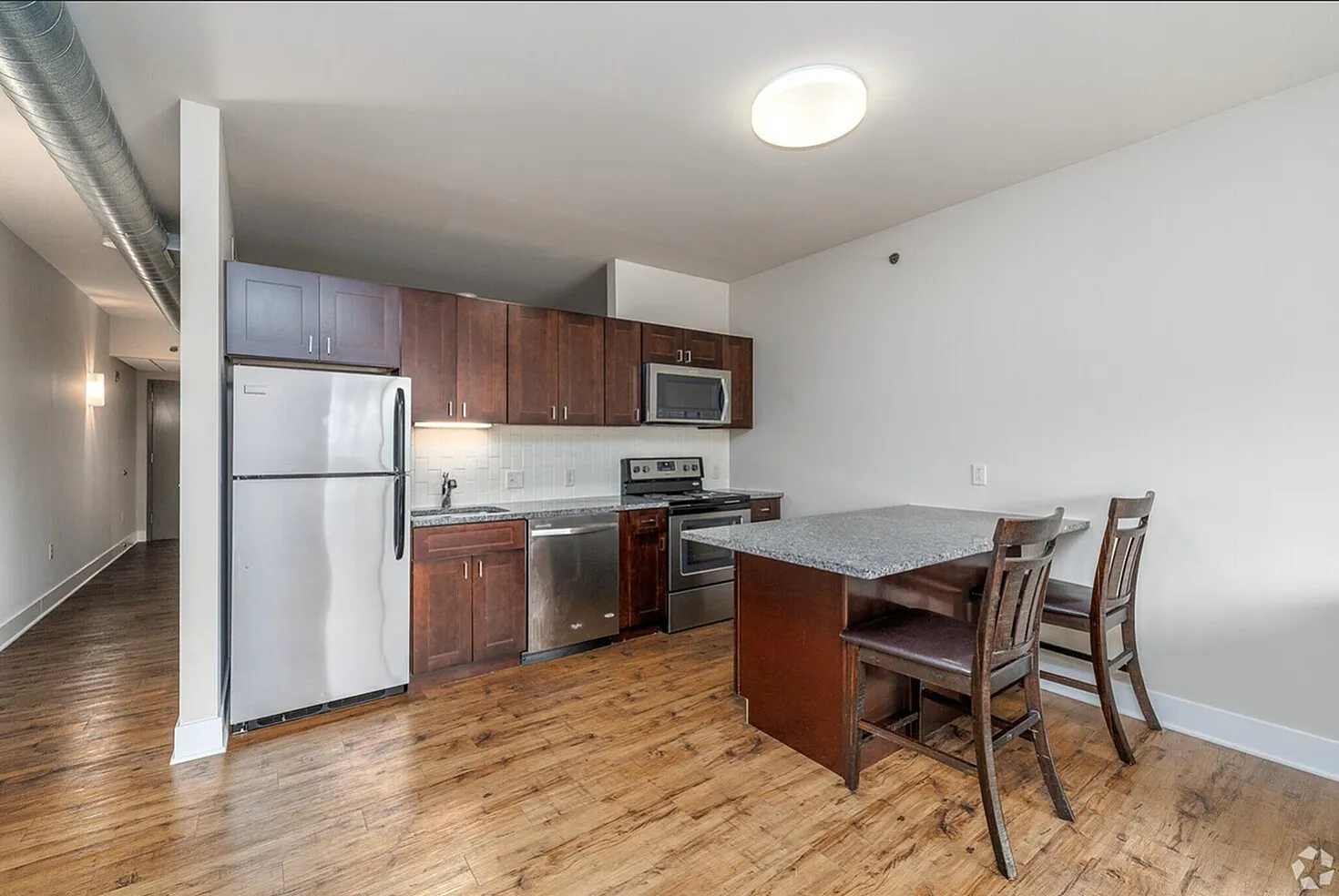 Modern kitchen with stainless steel appliances, cherry wood cabinets, and a sleek granite breakfast bar.