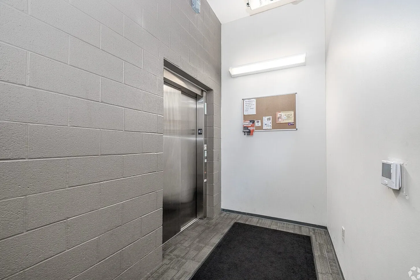 Modern apartment elevator lobby with sleek brushed metal doors, illuminated by bright overhead lighting, featuring a convenient bulletin board for community updates.