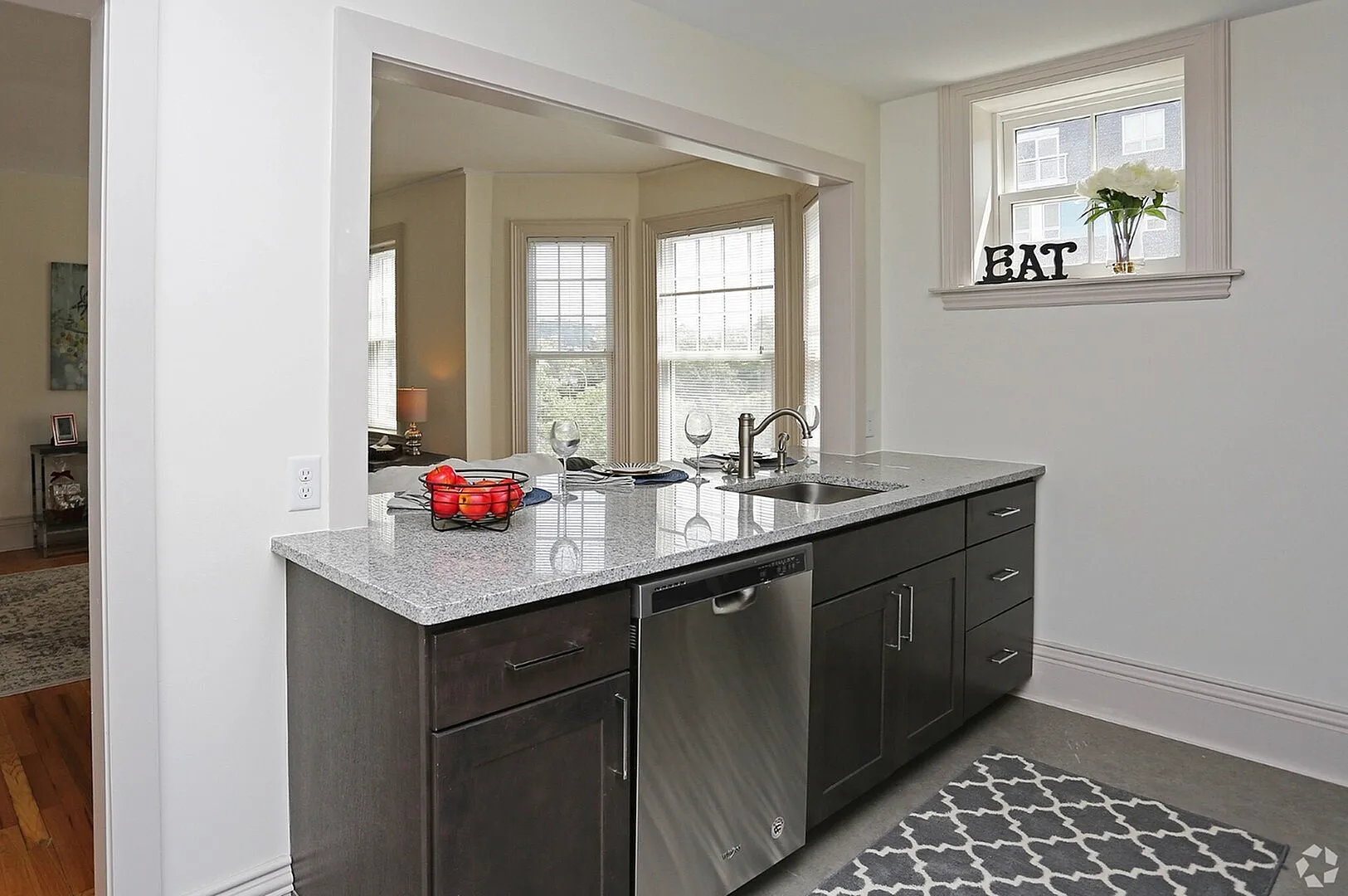 Bright kitchen with granite countertops, sleek dark cabinets, and a window view, seamlessly connected to the elegant dining area.
