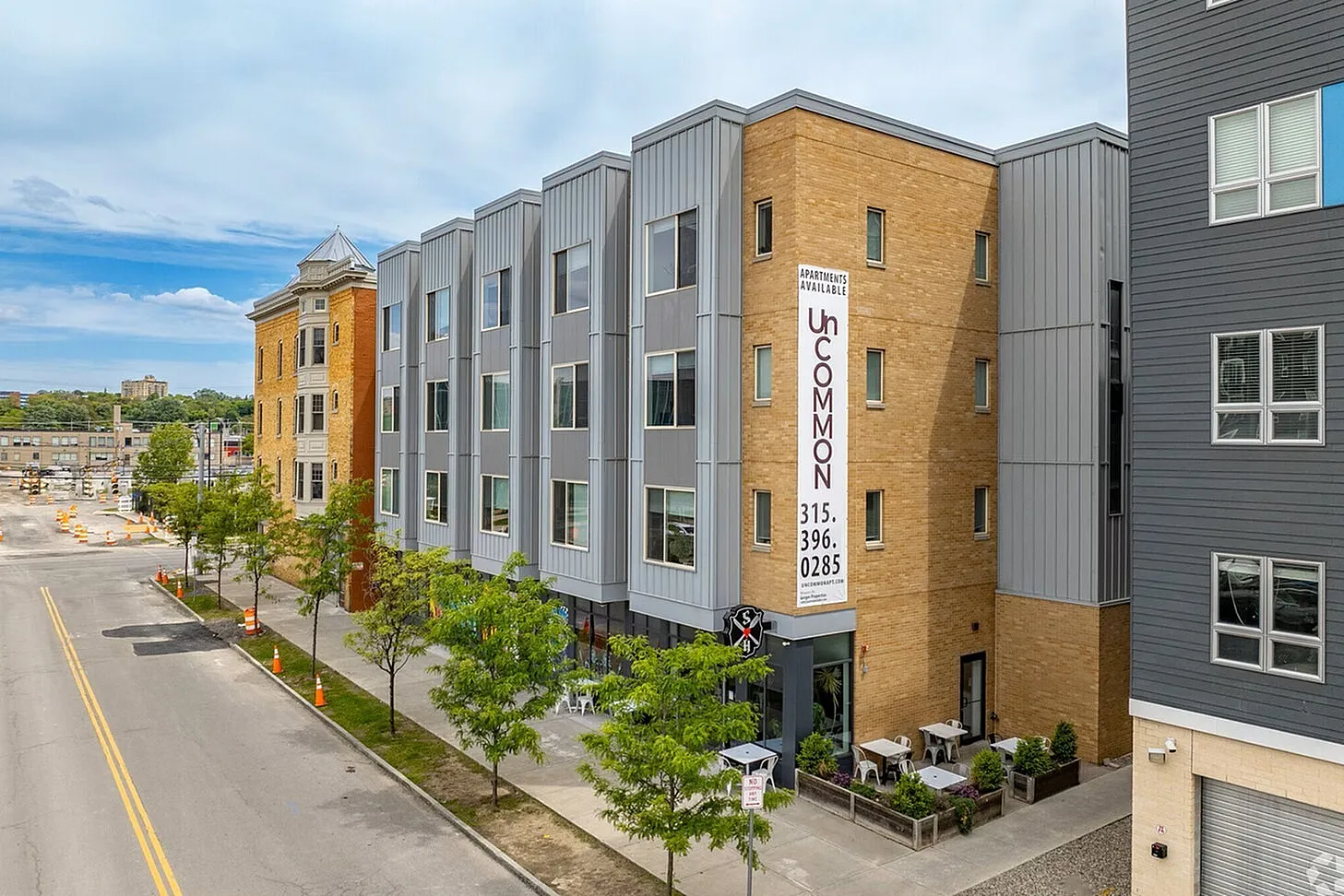 Modern urban apartment building with sleek architecture and street-level patio seating, showcasing vibrant city living.