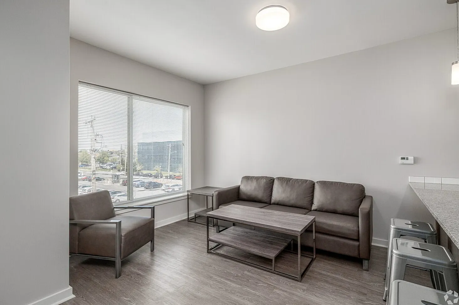 Bright and modern living area with sleek brown seating, large window with city view, and stylish furniture in an open-concept apartment.