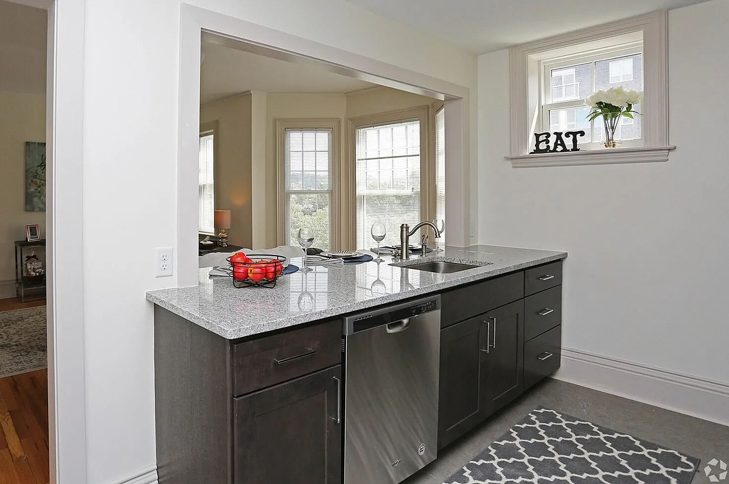 Elegant modern kitchen with sleek granite countertops, open view to a sunlit dining area, and contemporary stainless steel appliances.