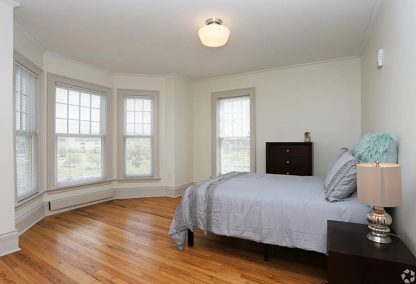 Bright and inviting bedroom with hardwood floors, elegant decor, and large bay windows allowing natural light to flood the space.