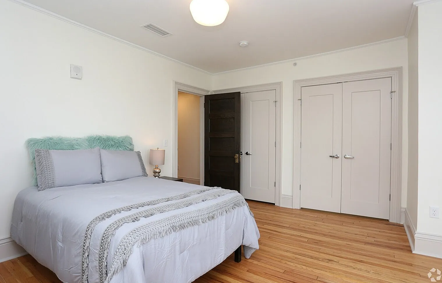 Inviting bedroom with sleek hardwood floors, soft grey bedding, and natural light, ideal for relaxation.