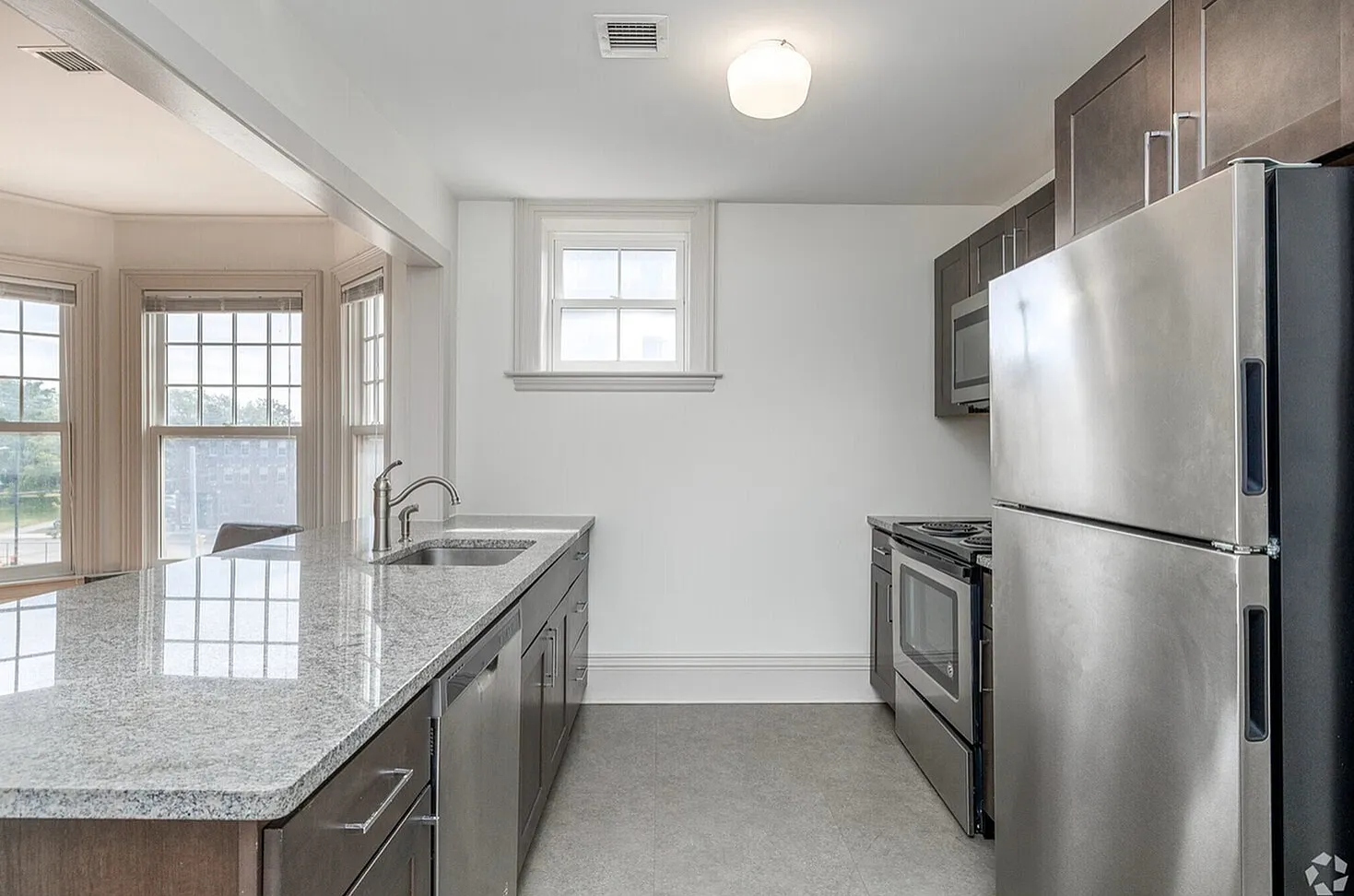Bright, modern kitchen with stainless steel appliances, chic dark cabinets, and expansive windows flooding the space with natural light.
