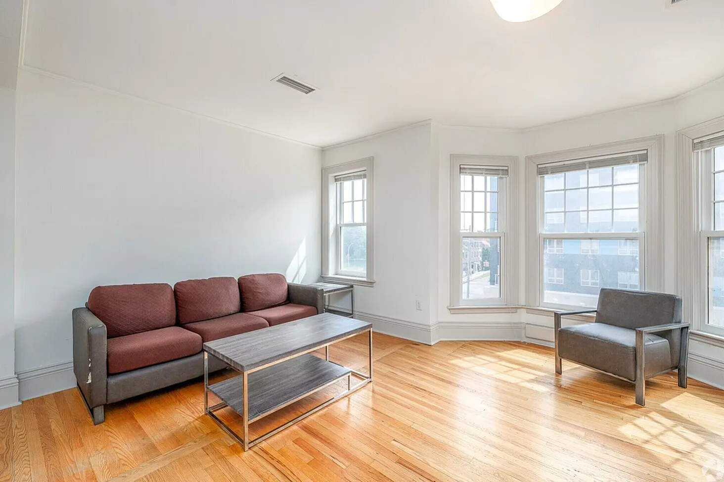 Bright and spacious living room with hardwood floors, cozy seating, and abundant natural light from large windows.