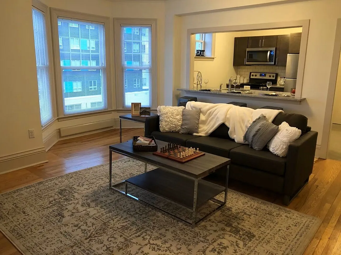 Charming living room with bay windows, elegant hardwood floors, a cozy sofa, and open kitchen with modern appliances.