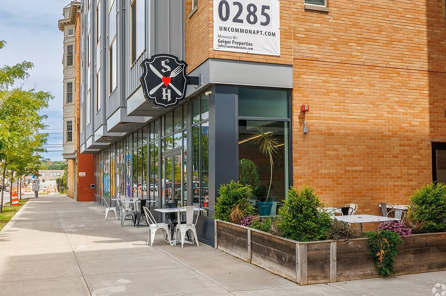 Charming street view showcasing modern apartment facade with stylish outdoor dining area and lush greenery.