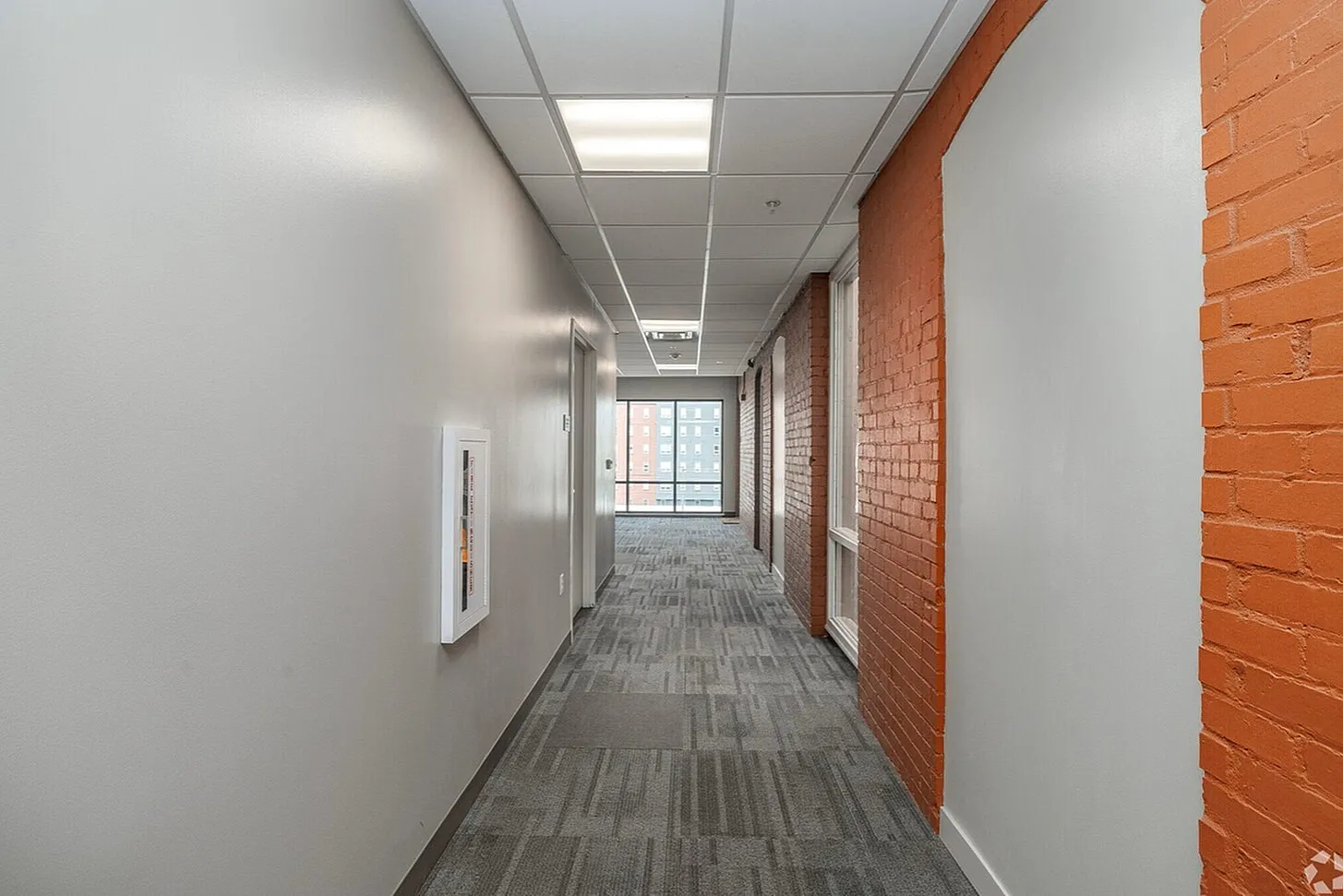 Bright and modern apartment hallway with stylish brick and white walls, leading to large windows at the end.