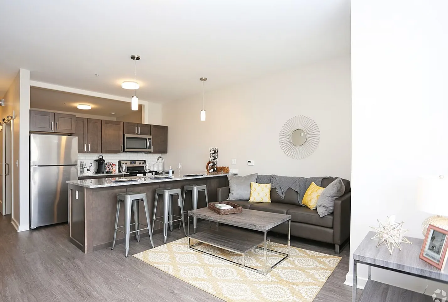 Contemporary open-plan living area with a sleek kitchen featuring stainless steel appliances, a cozy sofa with decorative pillows, and stylish modern decor.