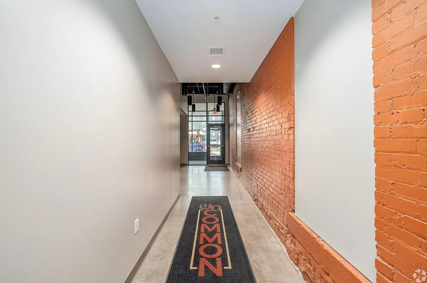 Chic industrial-style hallway with exposed brick and modern finishes, showcasing a welcoming entrance mat and sleek lighting.
