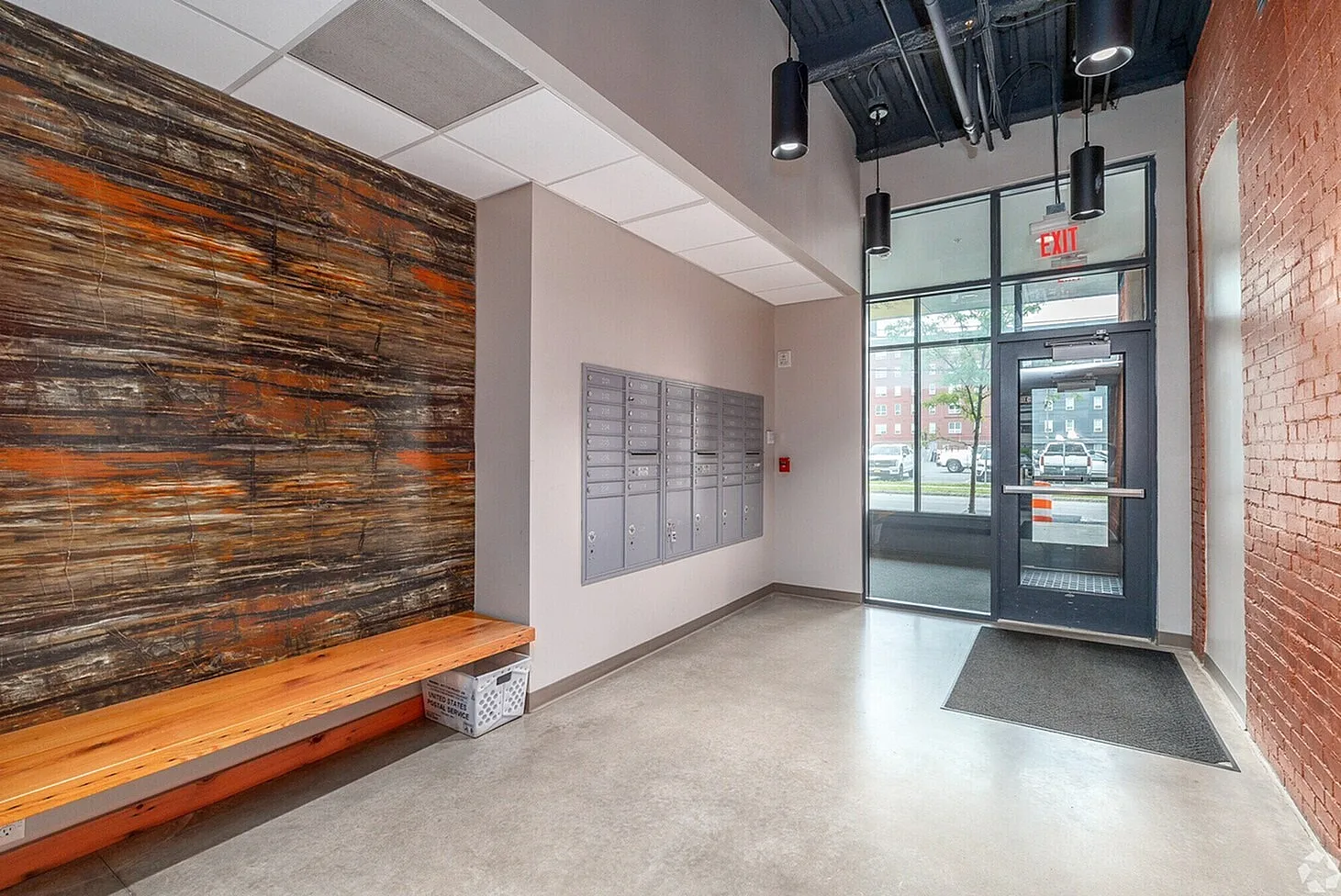 Modern apartment lobby with stylish wood accent wall, mailboxes, and glass entryway offering natural light.