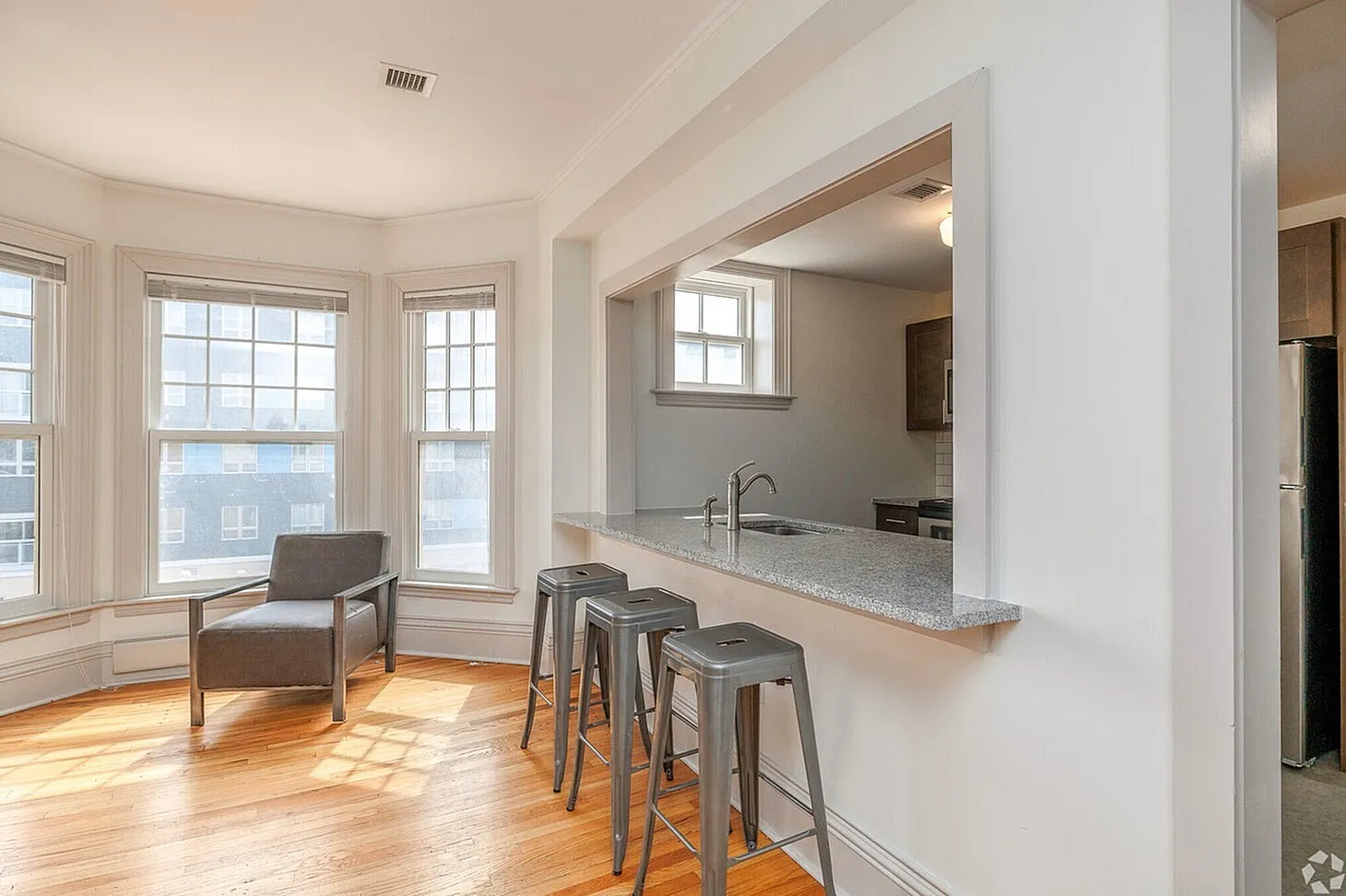 Bright and inviting living space featuring large windows, elegant hardwood floors, and a sleek breakfast bar with modern stools, perfect for entertaining.