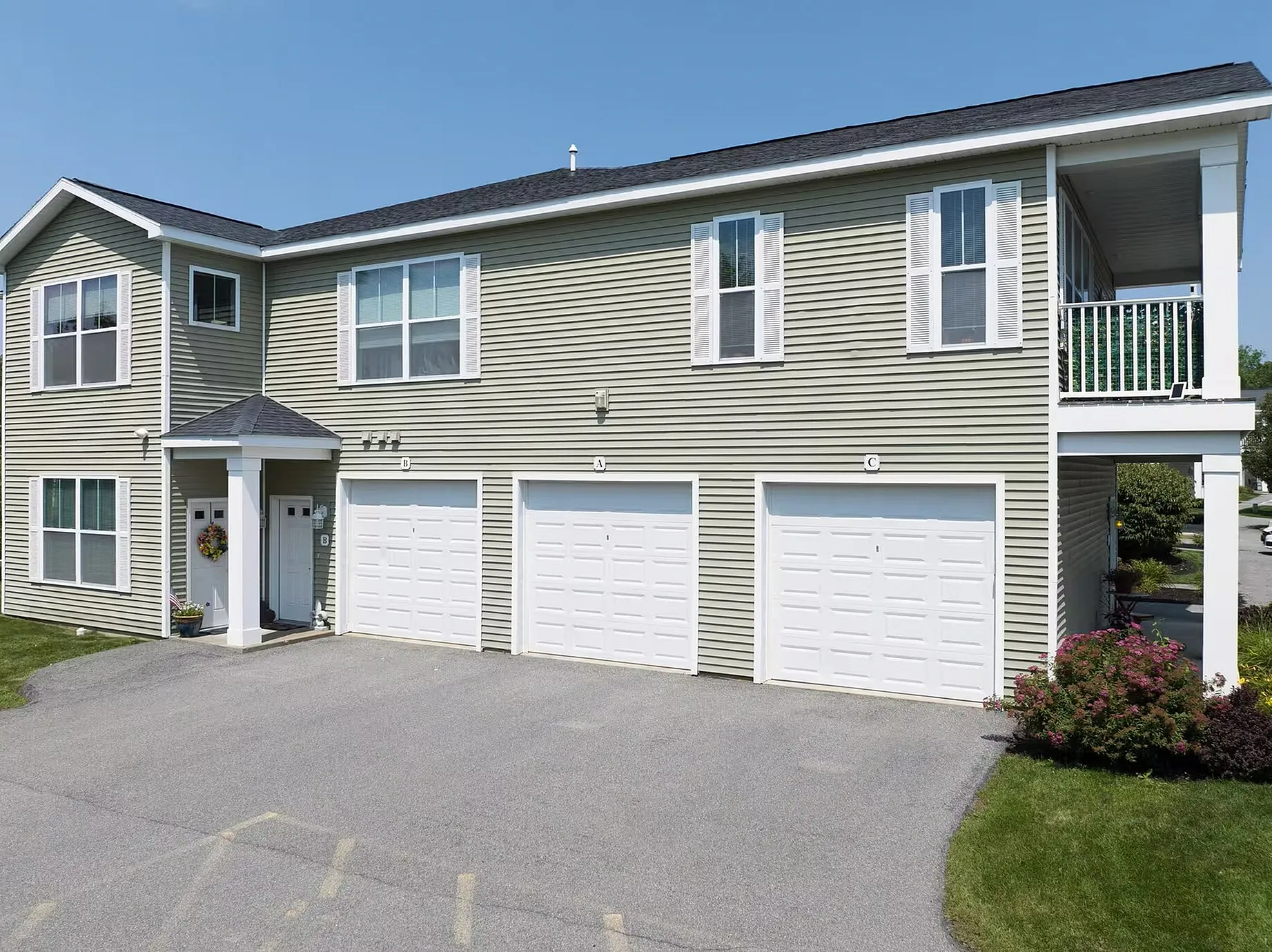 Modern apartment building with three white garage doors, stylish siding, and manicured landscaping, offering a welcoming residential ambiance.