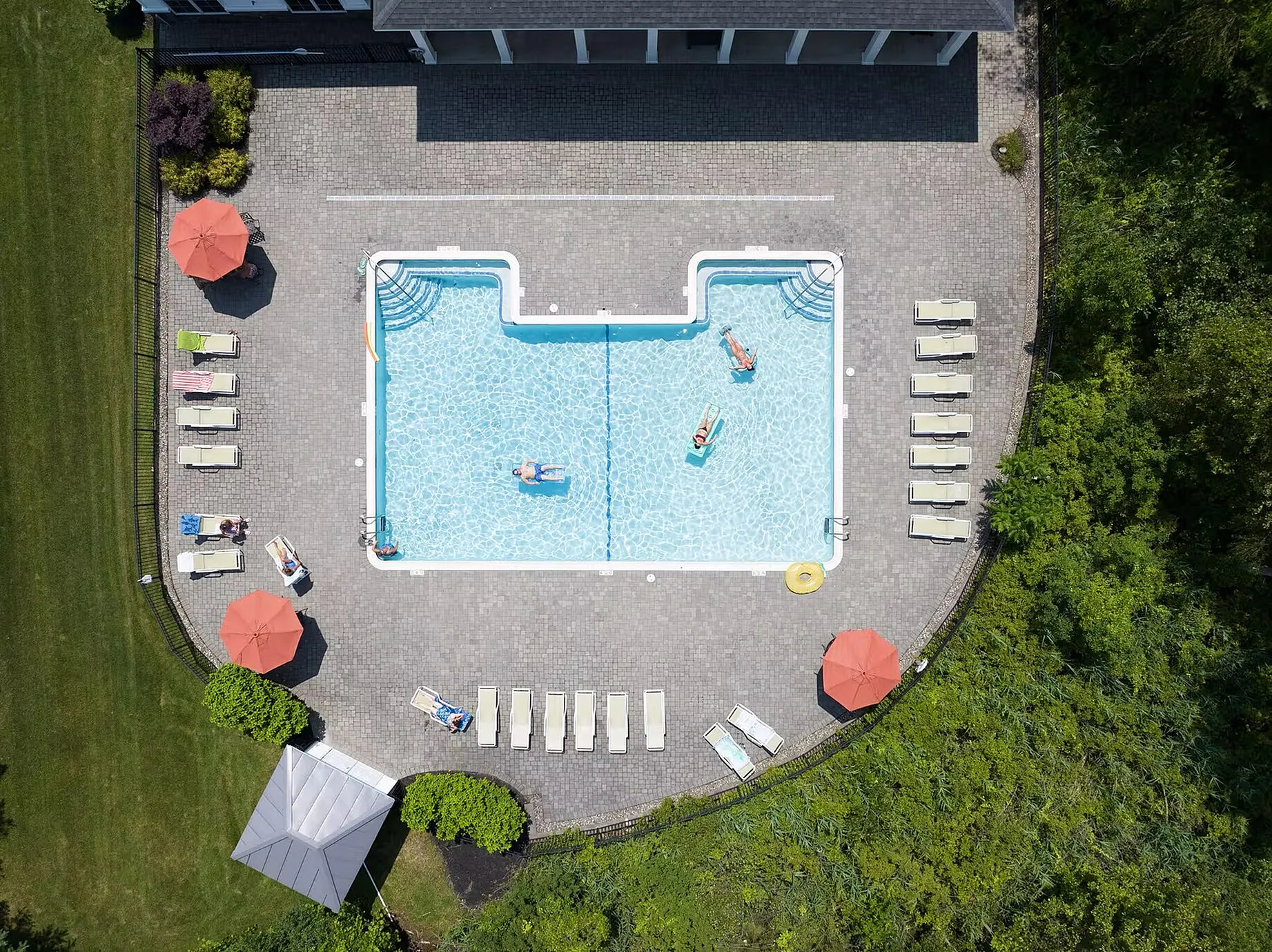 Aerial view of a luxurious outdoor pool with sun loungers, vibrant umbrellas, and lush greenery, perfect for relaxation and leisure.