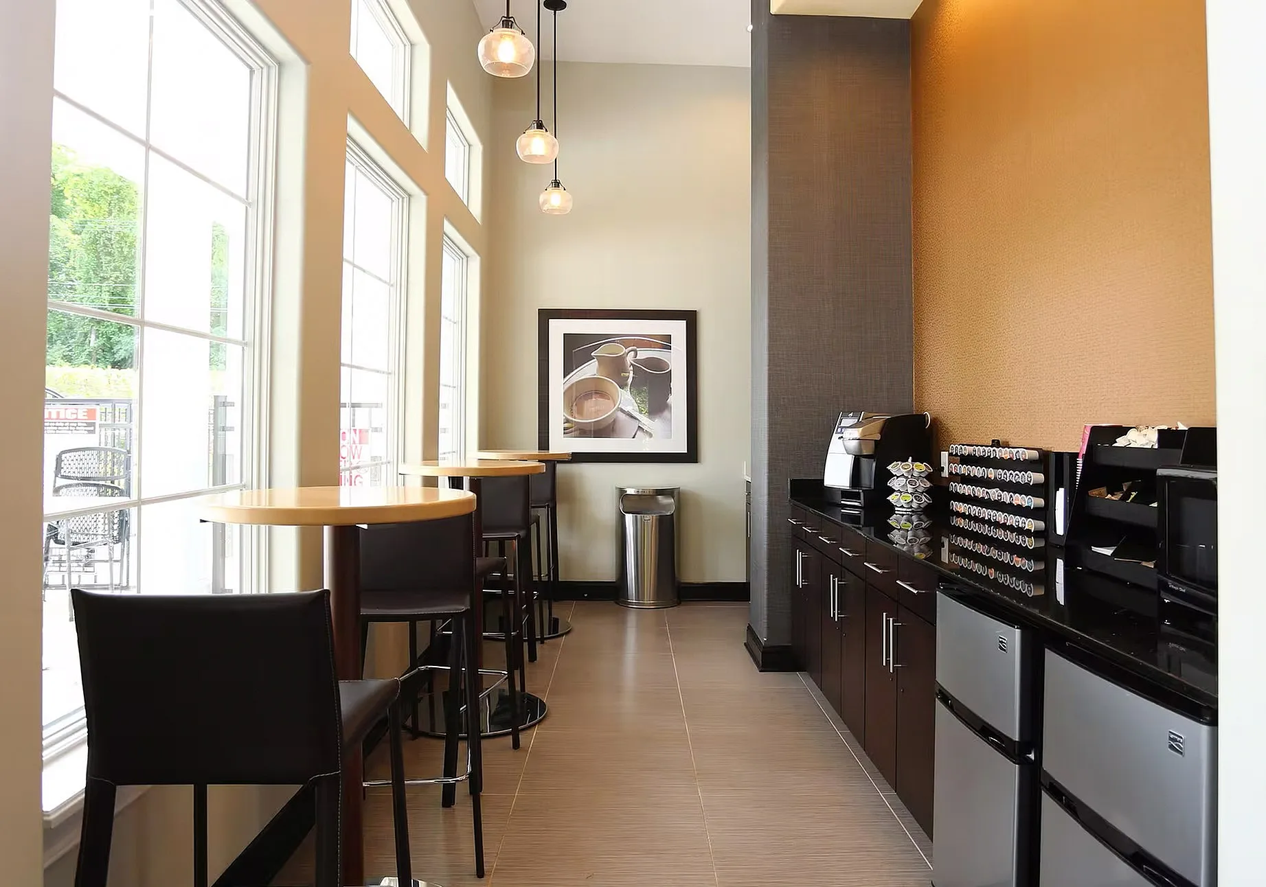 Modern coffee bar with sleek high-top tables, abundant natural light from tall windows, and stylish pendant lighting.
