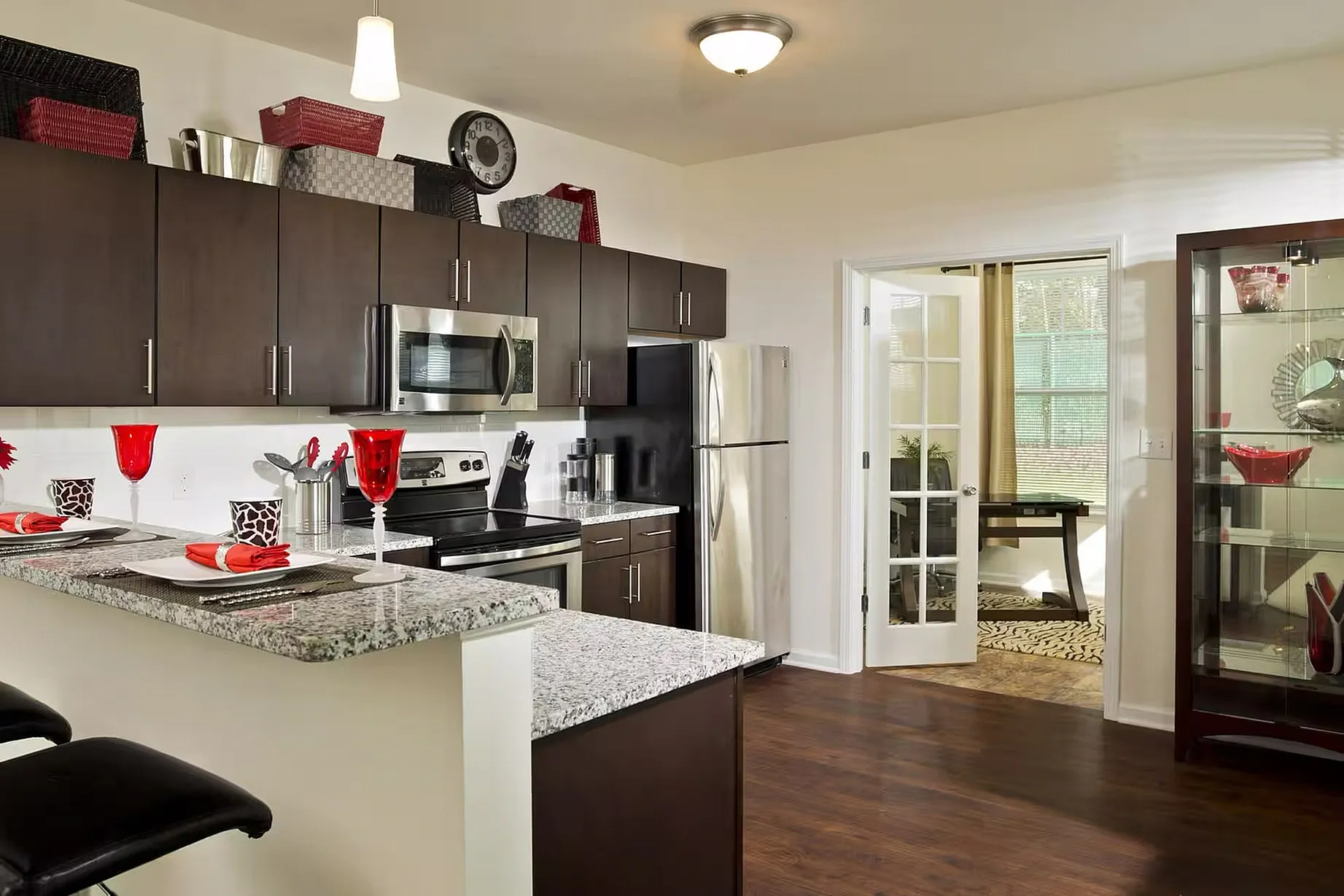 Modern kitchen with dark cabinetry, sleek appliances, and granite countertops, adjacent to a cozy dining area with elegant glassware and warm lighting.