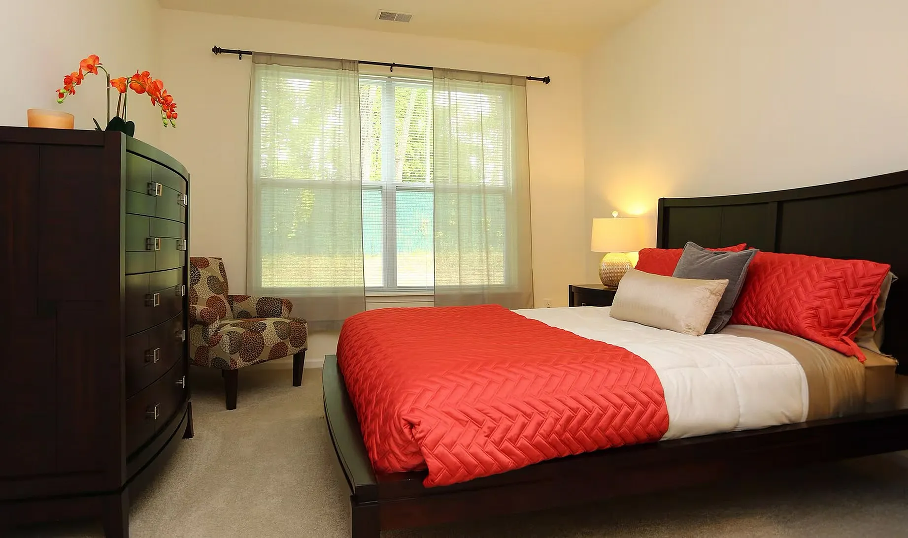 Inviting bedroom with a plush bed, vibrant orange accents, and a cozy chair, perfect for relaxation and comfort.