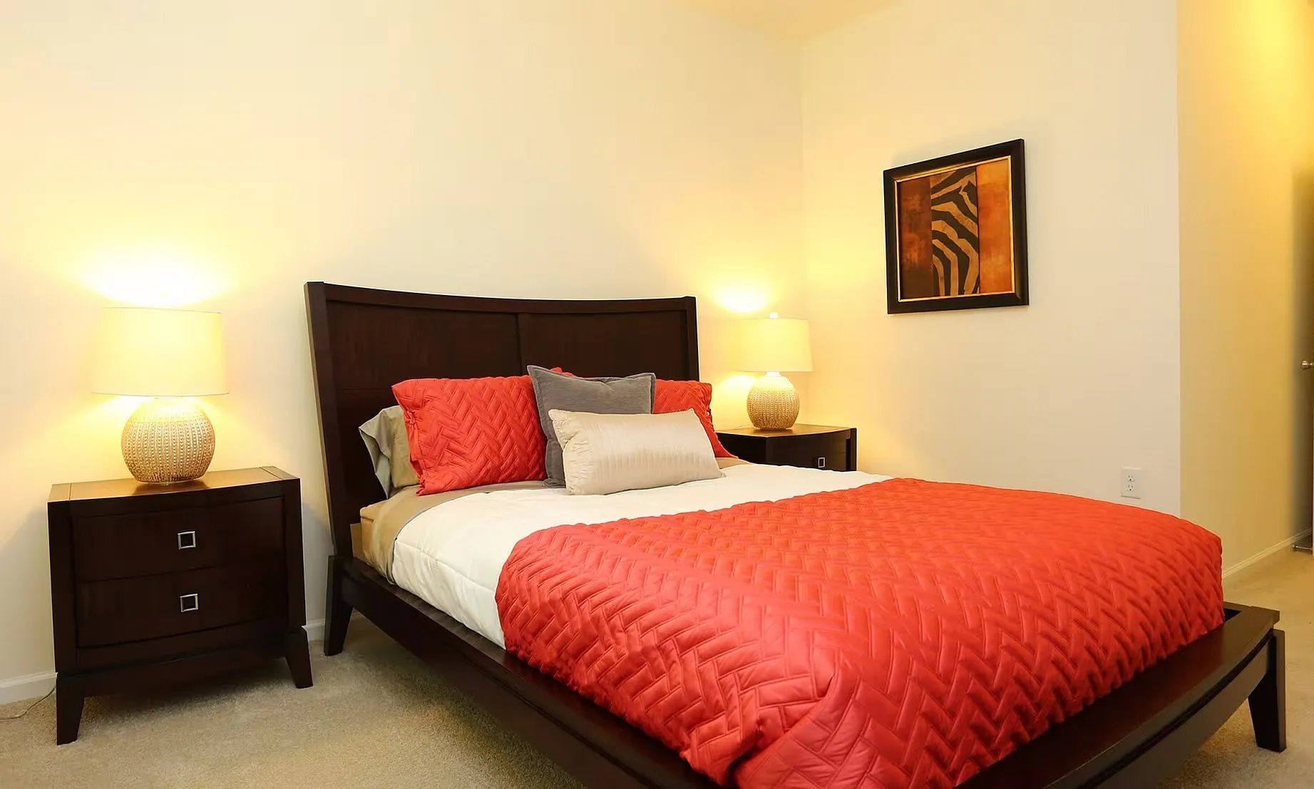 Cozy bedroom featuring a luxurious bed with vibrant orange bedding and elegant wooden furniture, illuminated by warm bedside lamps.