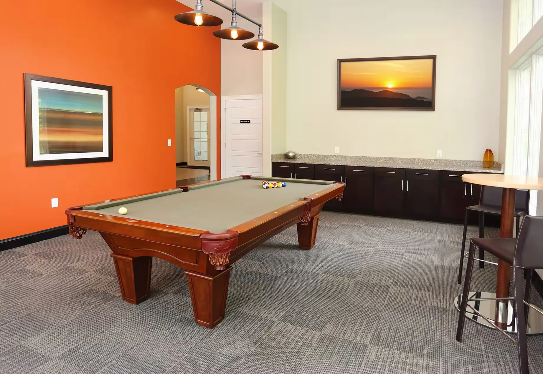 Modern recreation room with a wooden pool table, vibrant orange accent wall, and sleek cabinets, perfect for entertainment and relaxation.