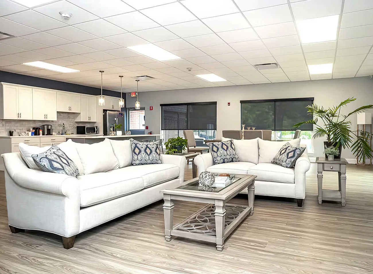 Bright and modern open-concept living room with stylish white sofas, elegant decor, and a sleek kitchen backdrop.