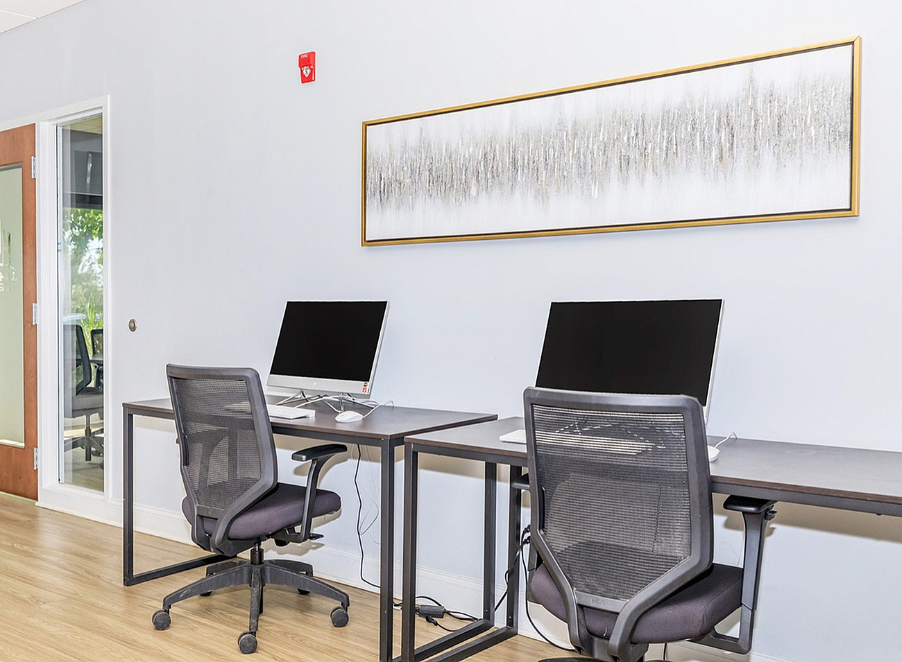 Modern workspace with two sleek computer stations, ergonomic chairs, and contemporary wall art, perfect for productivity.