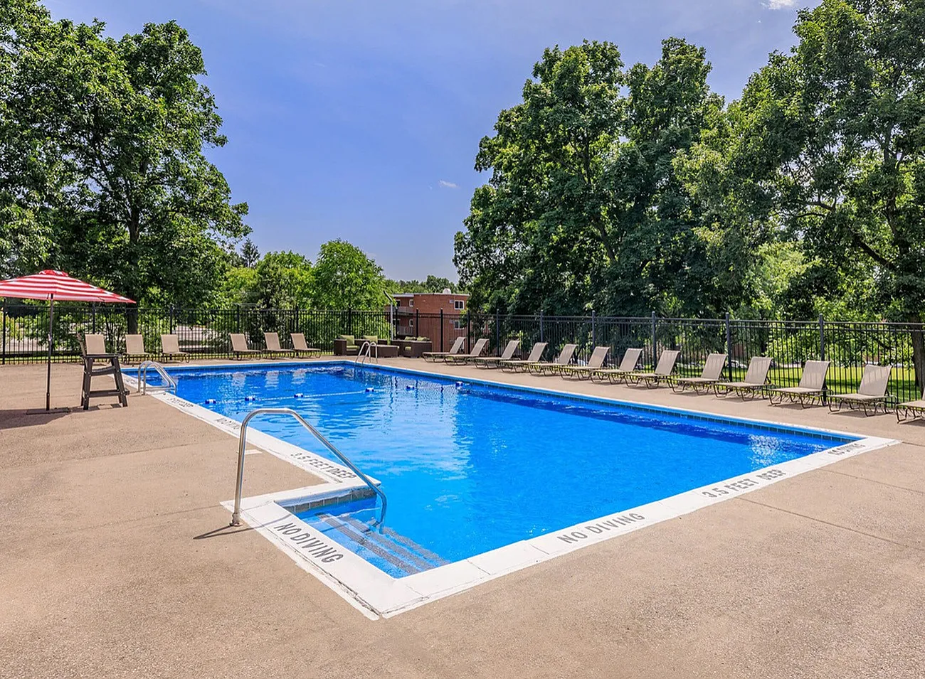 Inviting outdoor pool surrounded by lush greenery and stylish lounge chairs, perfect for relaxation and summer enjoyment.