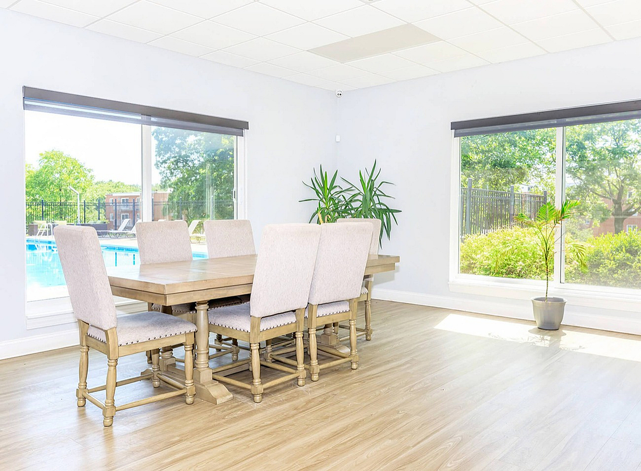 Bright dining area with elegant wooden table for eight, featuring large windows overlooking a lush garden and pool.