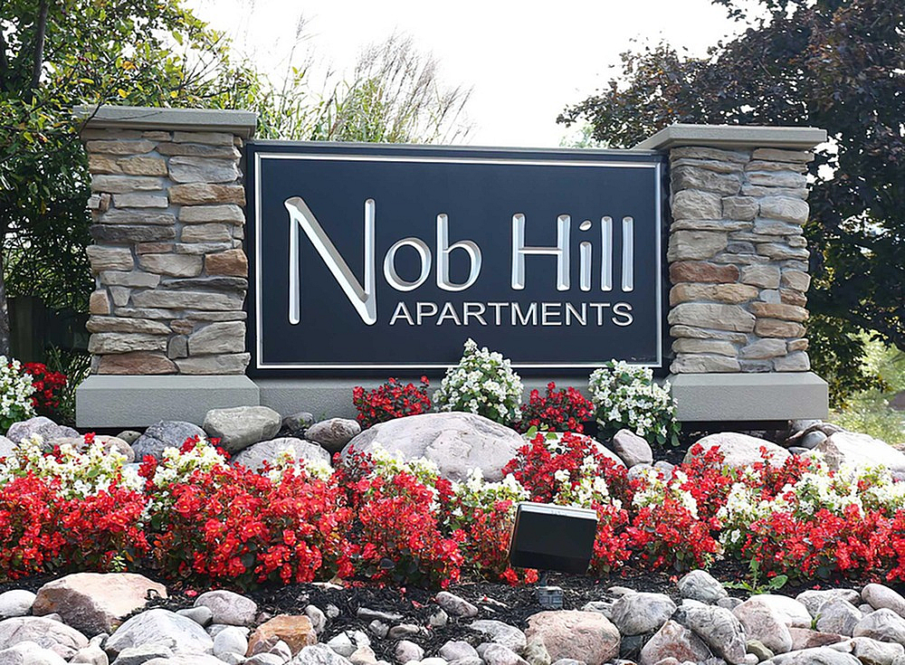 Welcoming entrance sign for Nob Hill Apartments, surrounded by vibrant red and white flowers and elegant stone pillars.