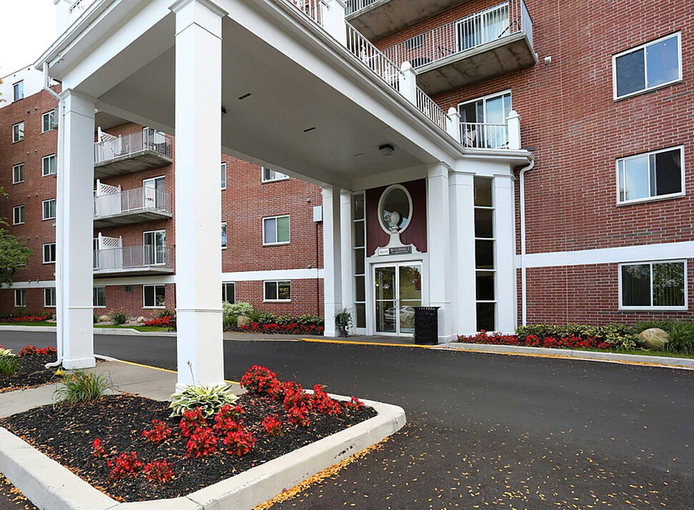 Elegant brick apartment building entrance with lush red flowerbeds and inviting balconies.
